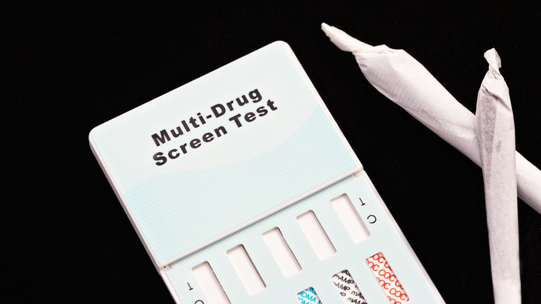 A multi-drug urine testing kit, designed for use at home, sits next to two hand-rolled marijuana cigarettes.