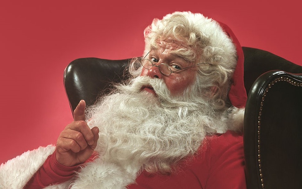 Portrait of Santa Claus sitting in a leather armchair raising one hand in a knowing gesture, 1980. United States. (Photo by T