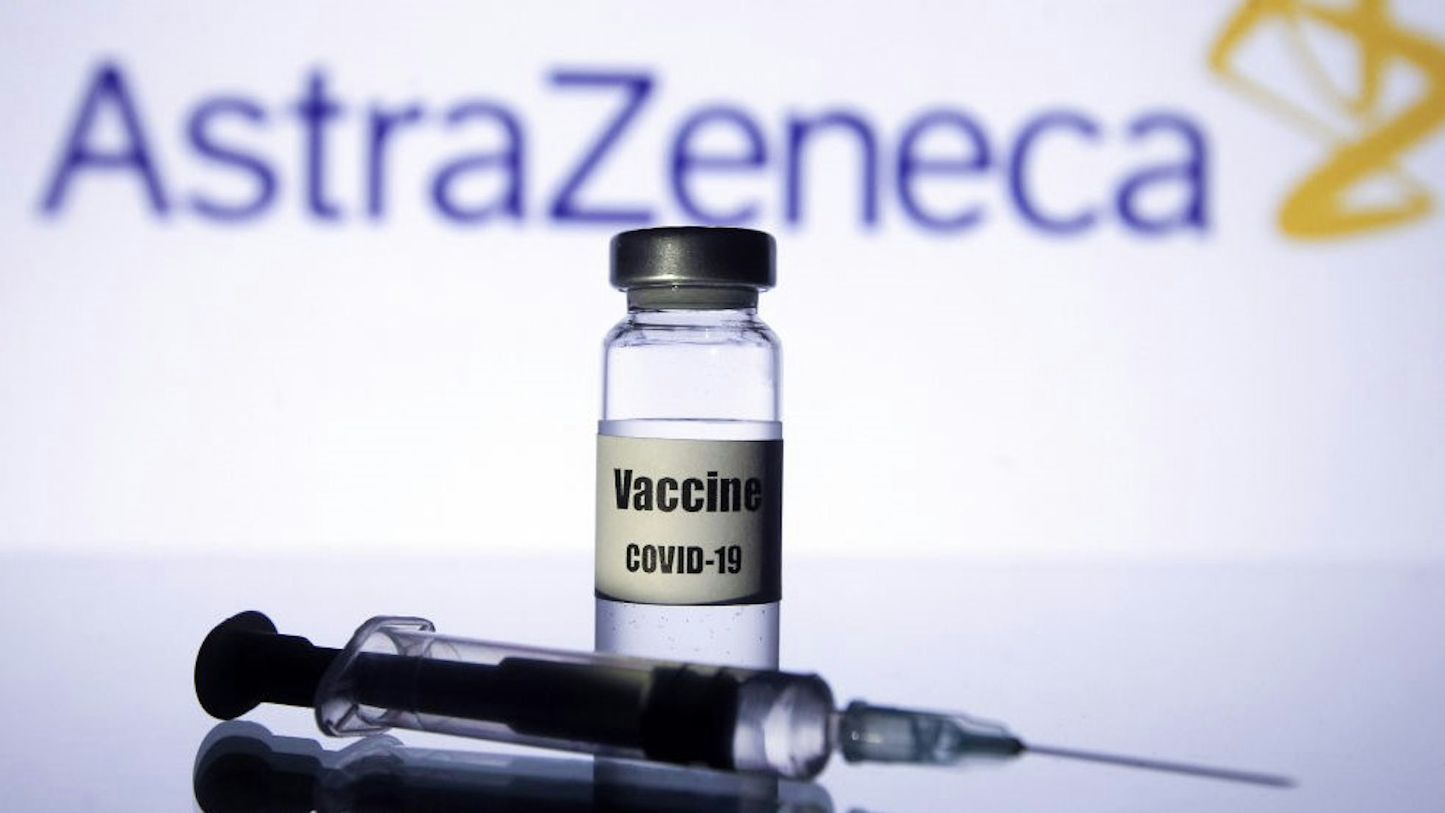 UKRAINE - 2020/11/21: In this photo illustration a medical syringe and a vial with COVID-19 coronavirus vaccine seen in front of the AstraZeneca biopharmaceutical company logo. (Photo Illustration by