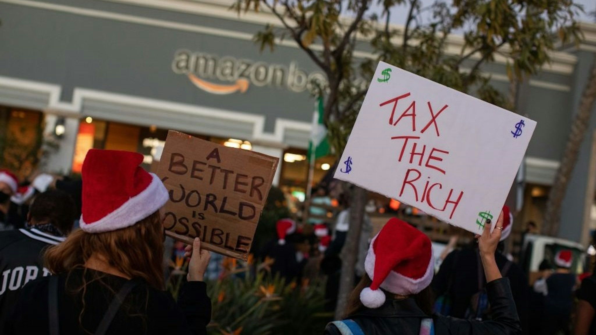Protesters wearing Santa's hats hold signs as they demonstrate in front of the Amazon Book Store in the Waterside shopping center in the Marina Del Rey neighborhood of Los Angeles during a Black Lives Matter rally to demand social justice on December 19, 2020.