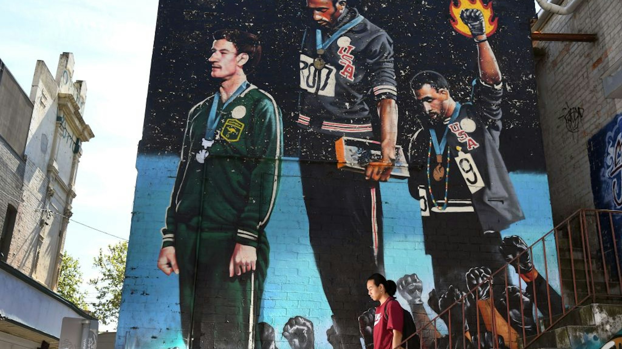 A photo taken in Melbourne on October 8, 2018, shows a man walking past a giant mural of Australian runner Peter Norman with US sprinters Tommie Smith and John Carlos.