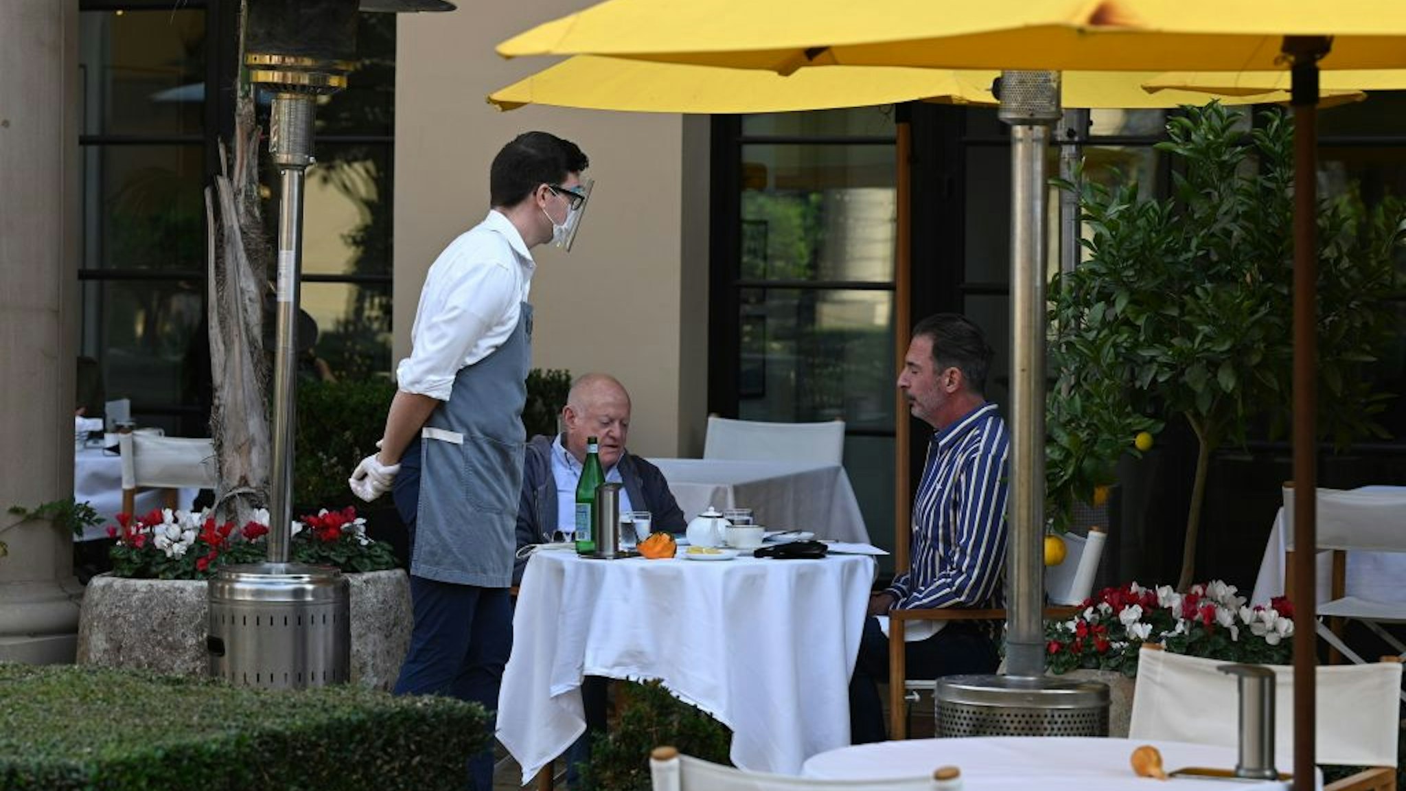 A server wearing a mask and face shield takes orders from customers at a restaurant in Beverly Hills, California, November 23, 2020. - Los Angeles County pubic health officials have issued an order to suspend all restaurant dining including outdoor dining for three weeks, starting November 24 at 10pm amid a surge of new coronavirus cases. There is major pushback against the order which some estimates will result in the loss of 700,000 jobs and lead to the closure of restaurants. (Photo by Robyn Beck / AFP) (Photo by ROBYN BECK/AFP via Getty Images)