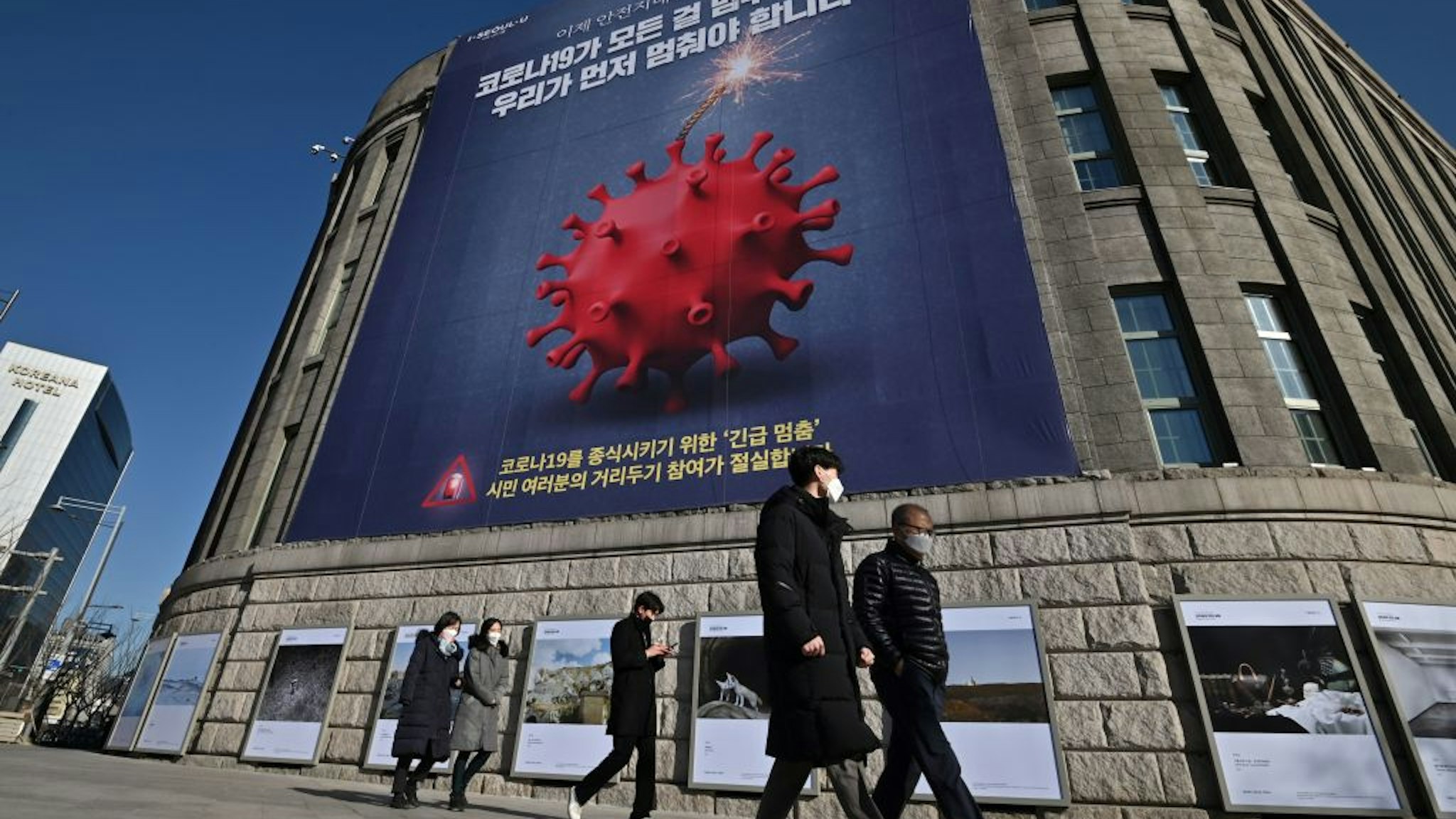 Pedestrians walk past a poster depicting the coronavirus as a bomb to warn against the covid-19 novel coronavirus at the city hall in Seoul on December 8, 2020.