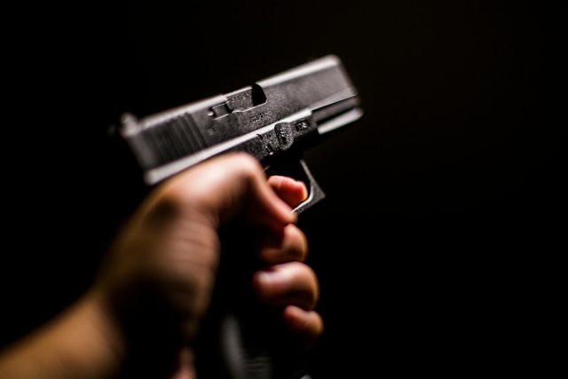 Cropped Hand Holding Gun Against Black Background - stock photo