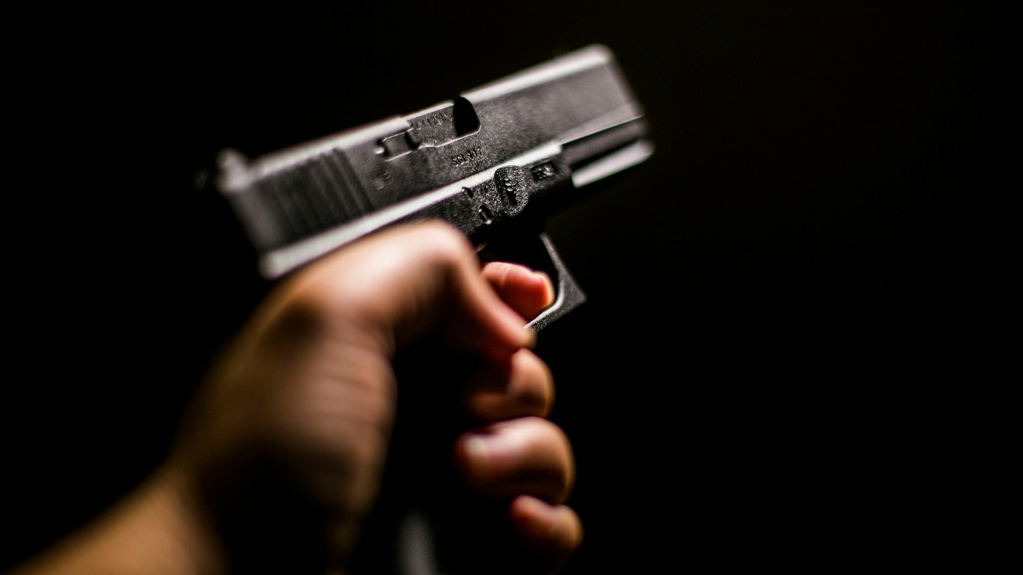 Cropped Hand Holding Gun Against Black Background - stock photo