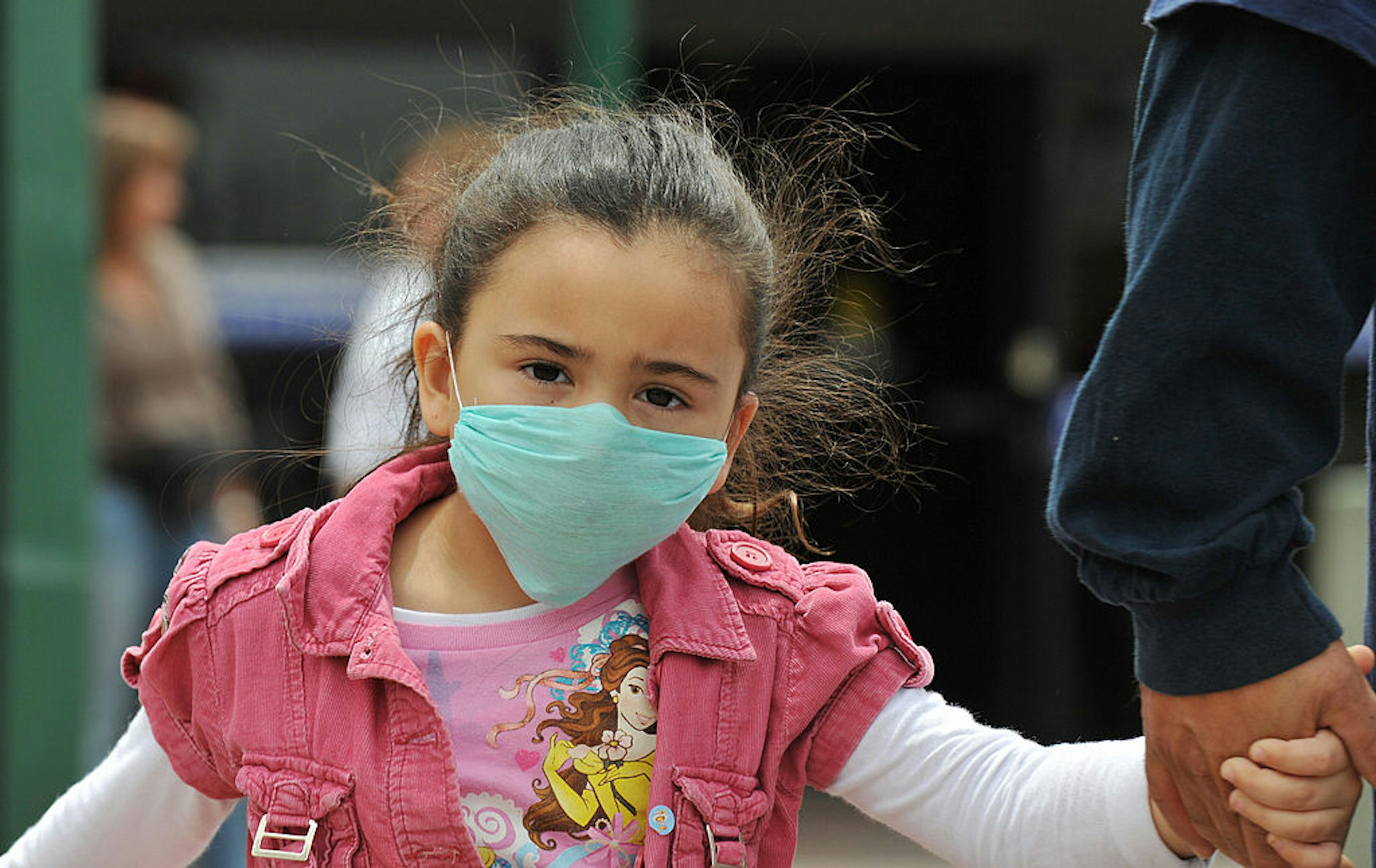 A girl, wearing a mask, holds her father's hand as they cross the international border between US and Mexico in San Ysidro, California, on April 27, 2009. The World Health Organization (WHO) raised its flu pandemic alert level from three to four, signalling a "significant increase in risk of a pandemic." The number of confirmed cases in the United States doubled to 40 on Monday, while Britain and Spain recorded their first swine flu victims. Mexico said the number of confirmed and suspected deaths from the flu had risen to 149, while some 1,600 people were thought to be infected. AFP PHOTO/Jewel SAMAD (Photo credit should read JEWEL SAMAD/AFP via Getty Images)