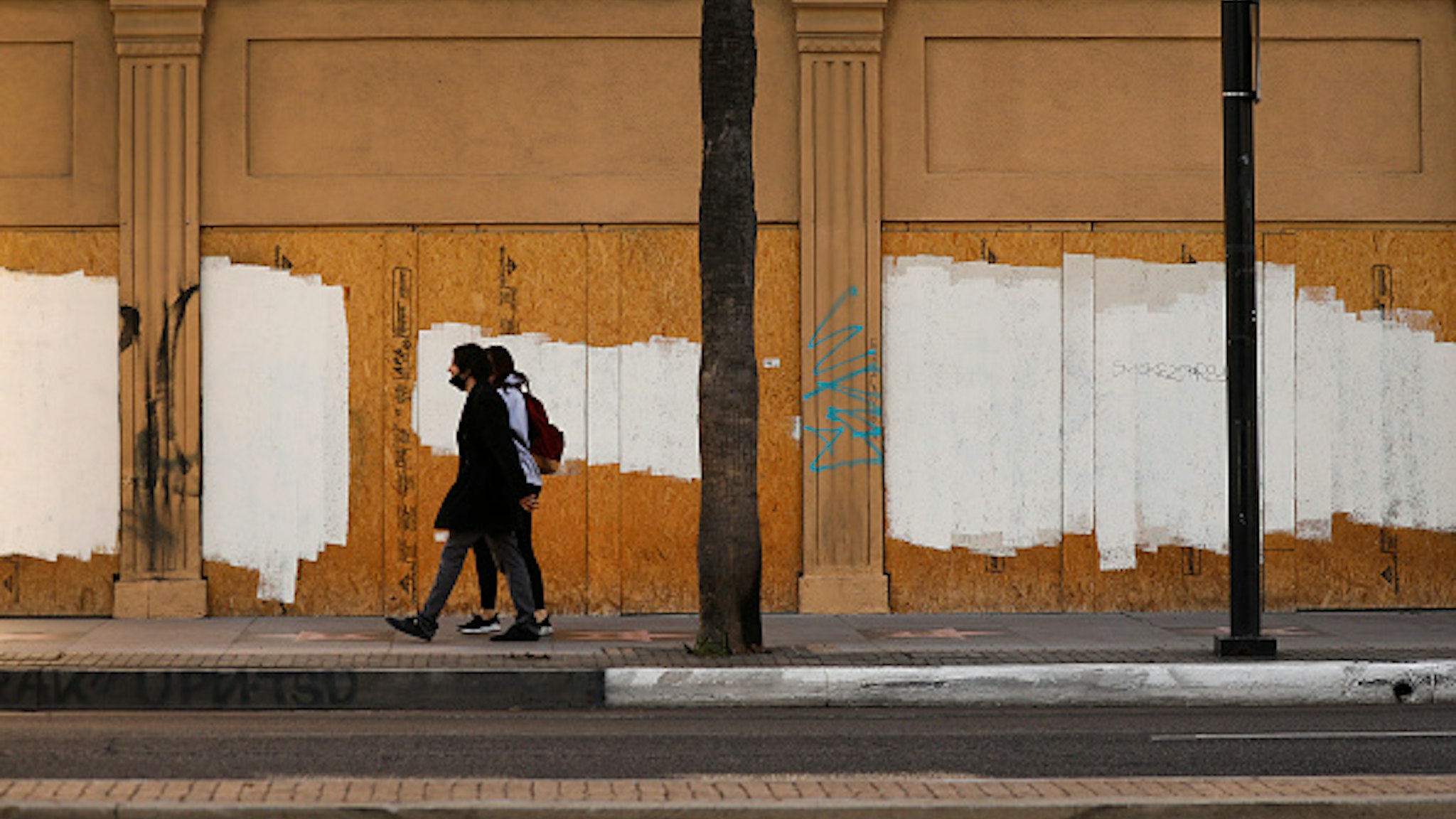 LOS ANGELES, CA - DECEMBER 02: Pedestrians walk past boarded windows of a building on Hollywood Blvd and North Sycamore Ave in Hollywood which is close to Rochelle Begaye, 42, who has created a complex nearby stitched together with plywood, bed frames, and various fencing materials to create a encampment of tents covered with discarded plastic and tarps located on a sliver of land at the corner of Hollywood at La Brea containing the Four Ladies of Hollywood. Hollywood on Wednesday, Dec. 2, 2020 in Los Angeles, CA