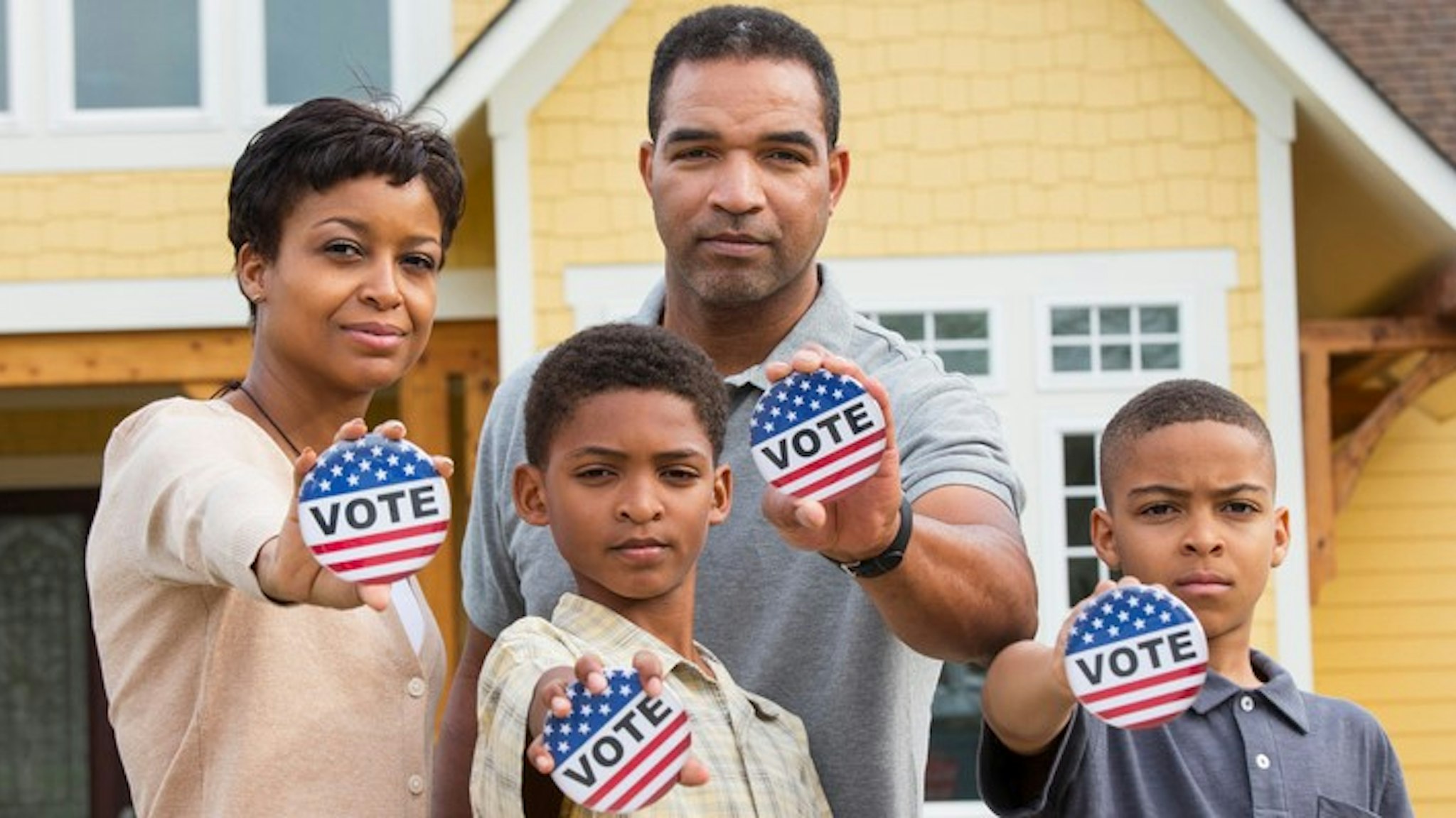 Black family holding Vote buttons outside home