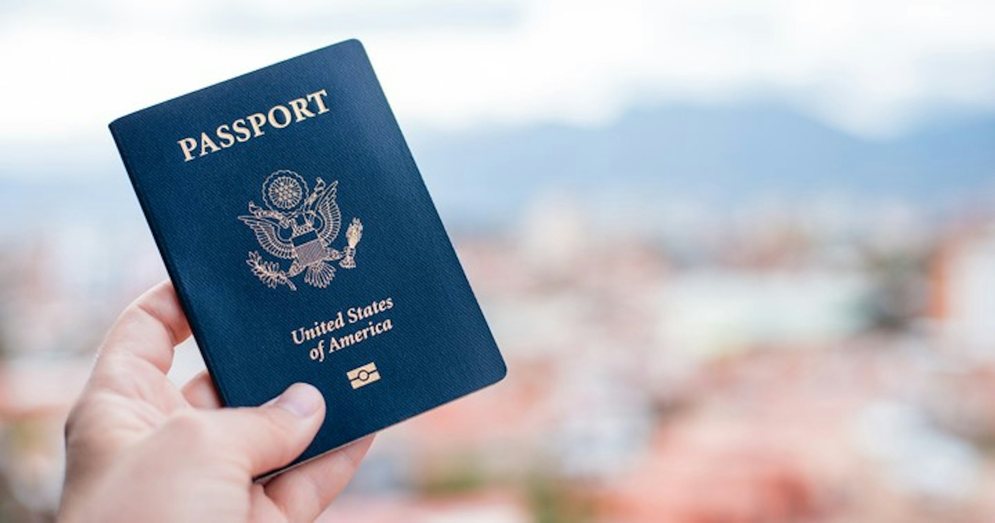 Close-Up Of Hand Holding American Passport Against Townscape