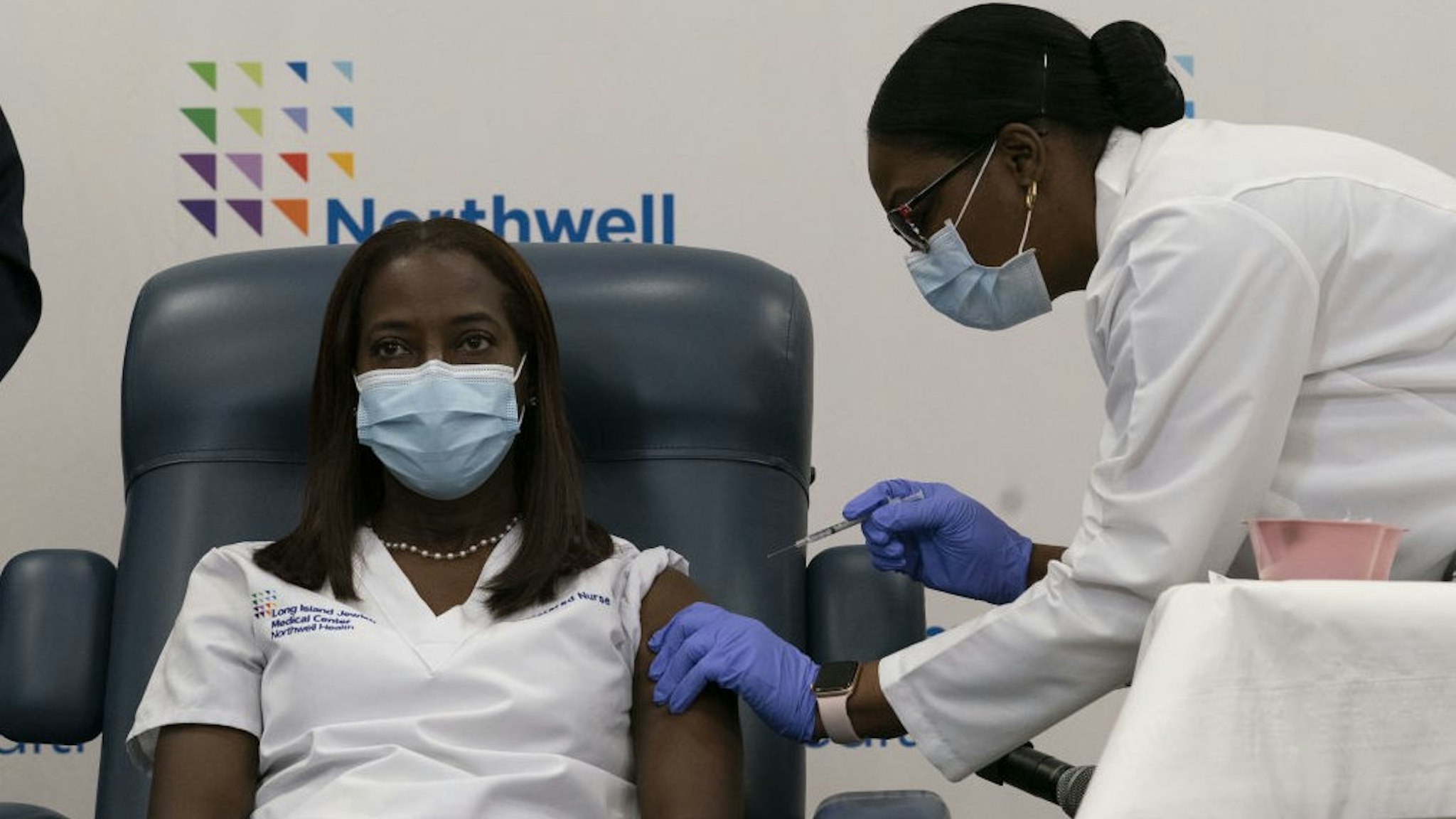 Healthcare worker Sandra Lindsay, left, receives the Pfizer-BioNTech Covid-19 vaccine from Dr. Michelle Chester at the Northwell Health Long Island Jewish Medical Center in the Queens borough of New York, U.S., on Monday, Dec. 14, 2020. The first Covid-19 vaccine shots were administered by U.S. hospitals Monday, the initial step in a historic drive to immunize millions of people as deaths approach the 300,000 mark. Photographer: