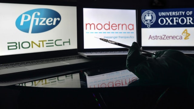 An illustrative photo showing a medical syringe seen in front of Pfizer-BionTech, Moderna and AstraZeneca-University of Oxford logos displayed on screens in the background on Christmas Eve. On Thursday, December 24, 2020, in Dublin, Ireland. (Photo illustration by