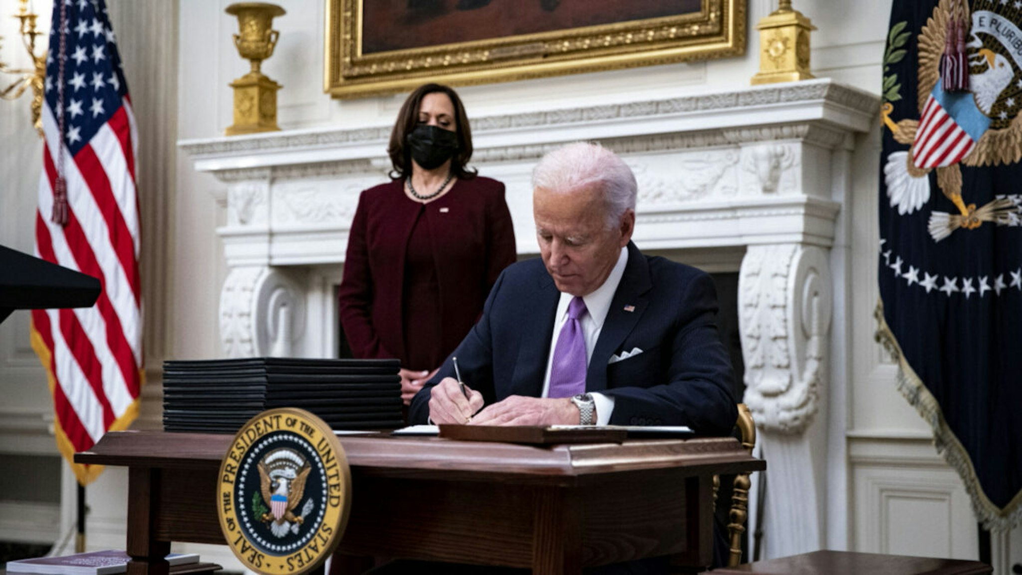 U.S. President Joe Biden signs an executive order after speaking during an event on his administration's Covid-19 response with U.S. Vice President Kamala Harris, left, in the State Dining Room of the White House in Washington, D.C., U.S., on Thursday, Jan. 21, 2021.