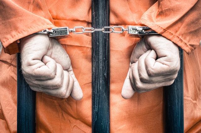 Close-Up Of Man With Handcuffs Standing In Prison - stock photo