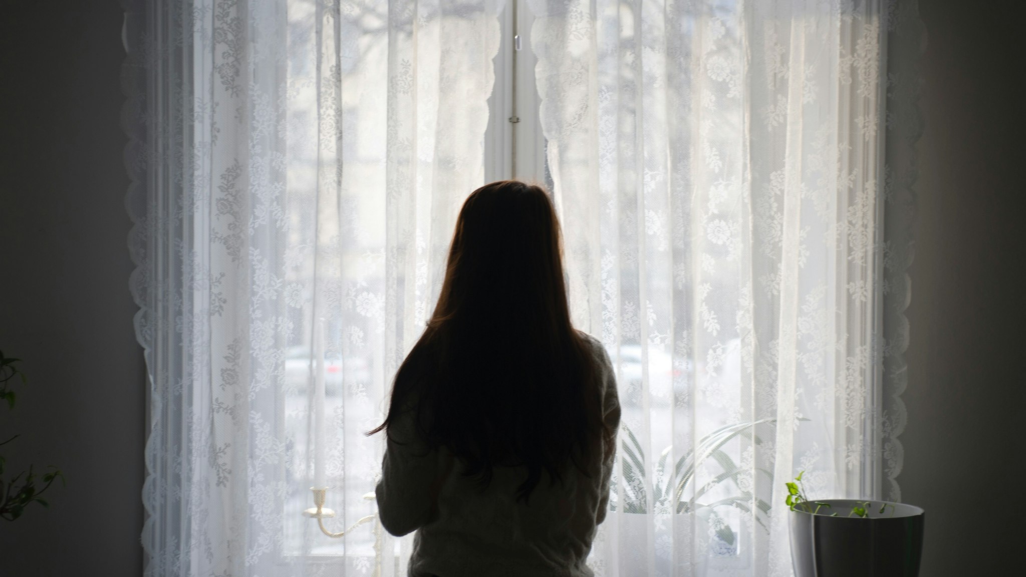 Rear View Of Woman Looking Through Window While Standing At Home - stock photo