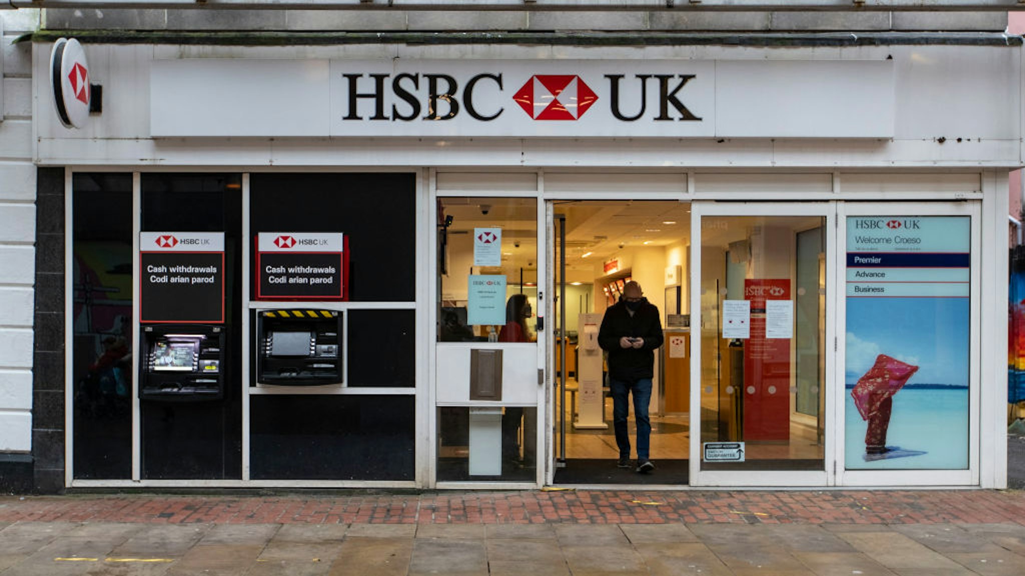 A man wearing a face mask walks out of the HSBC UK bank.