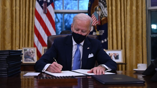TOPSHOT - US President Joe Biden sits in the Oval Office as he signs a series of orders at the White House in Washington, DC, after being sworn in at the US Capitol on January 20, 2021. - US President Joe Biden signed a raft of executive orders to launch his administration, including a decision to rejoin the Paris climate accord. The orders were aimed at reversing decisions by his predecessor, reversing the process of leaving the World Health Organization, ending the ban on entries from mostly Muslim-majority countries, bolstering environmental protections and strengthening the fight against Covid-19.