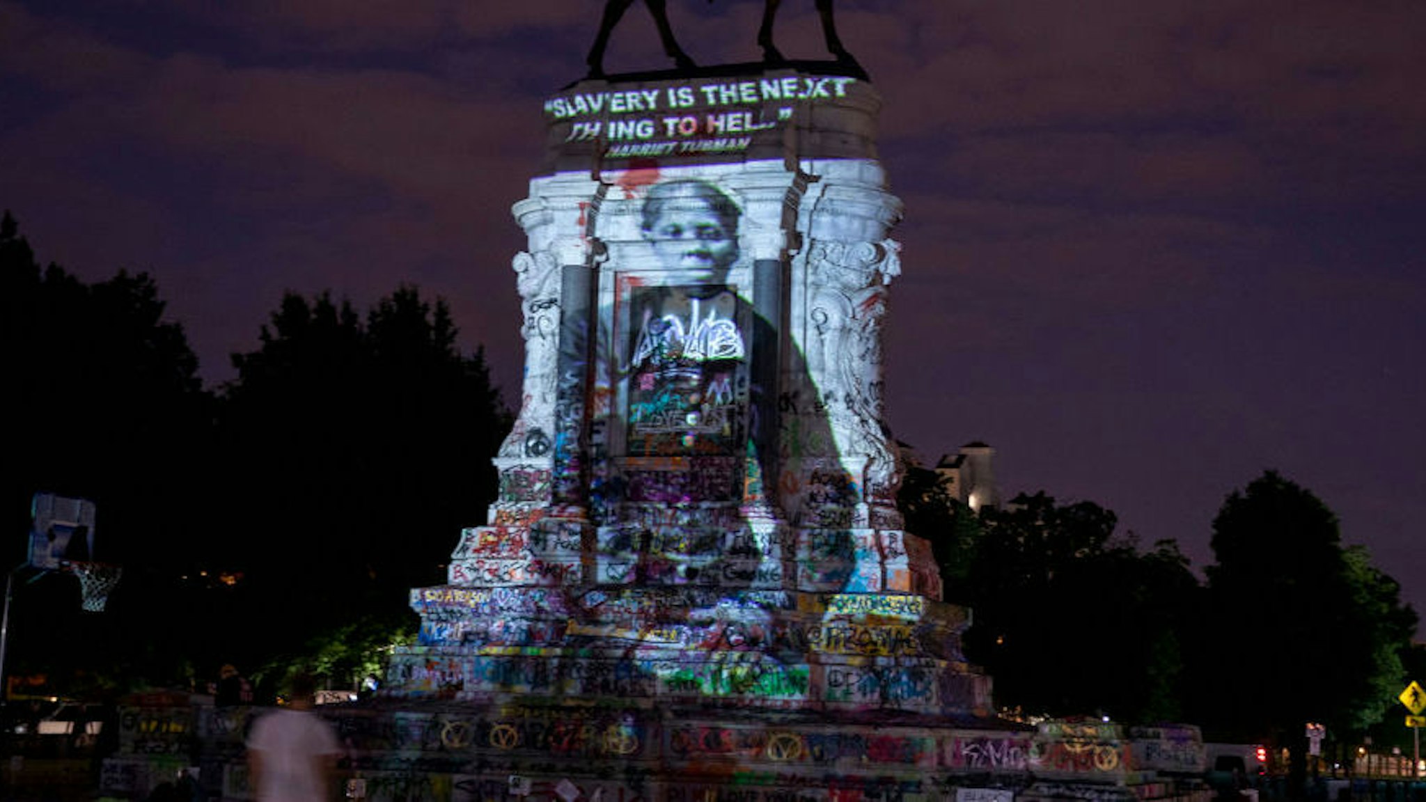 RICHMOND, VIRGINIA - JUNE 18: Harriet Tubman's image is projected on the Robert E. Lee Monument as people gather around on June 18, 2020 in Richmond, Virginia. Richmond Circuit Court Judge Bradley Cavedo ruled on Thursday to indefinitely extended an injunction preventing the Virginia governor from removing a historic statue of Confederate Gen. Robert E. Lee from Richmond's famed Monument Avenue (Photo by Tasos Katopodis/Getty Images)