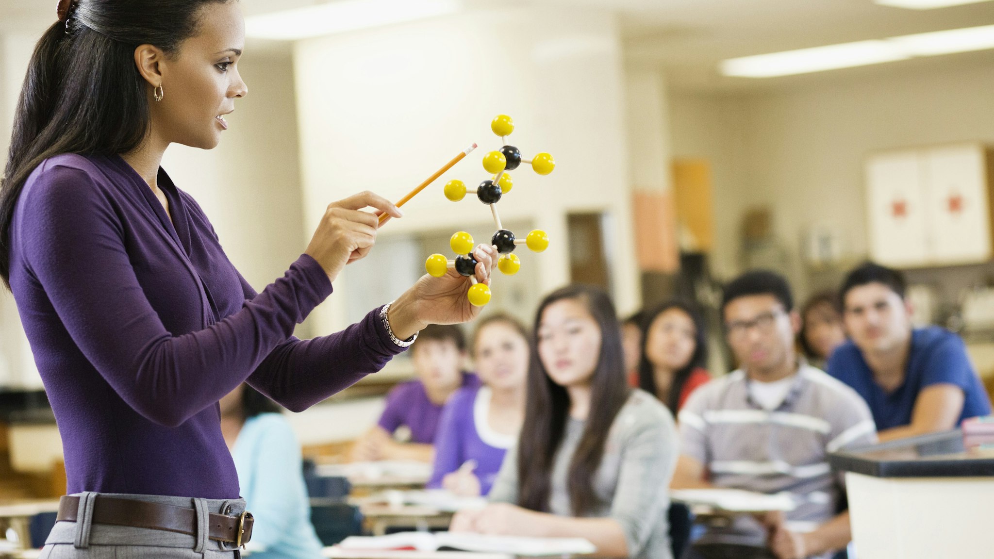 Teacher explaining chemistry model to classroom - stock photo