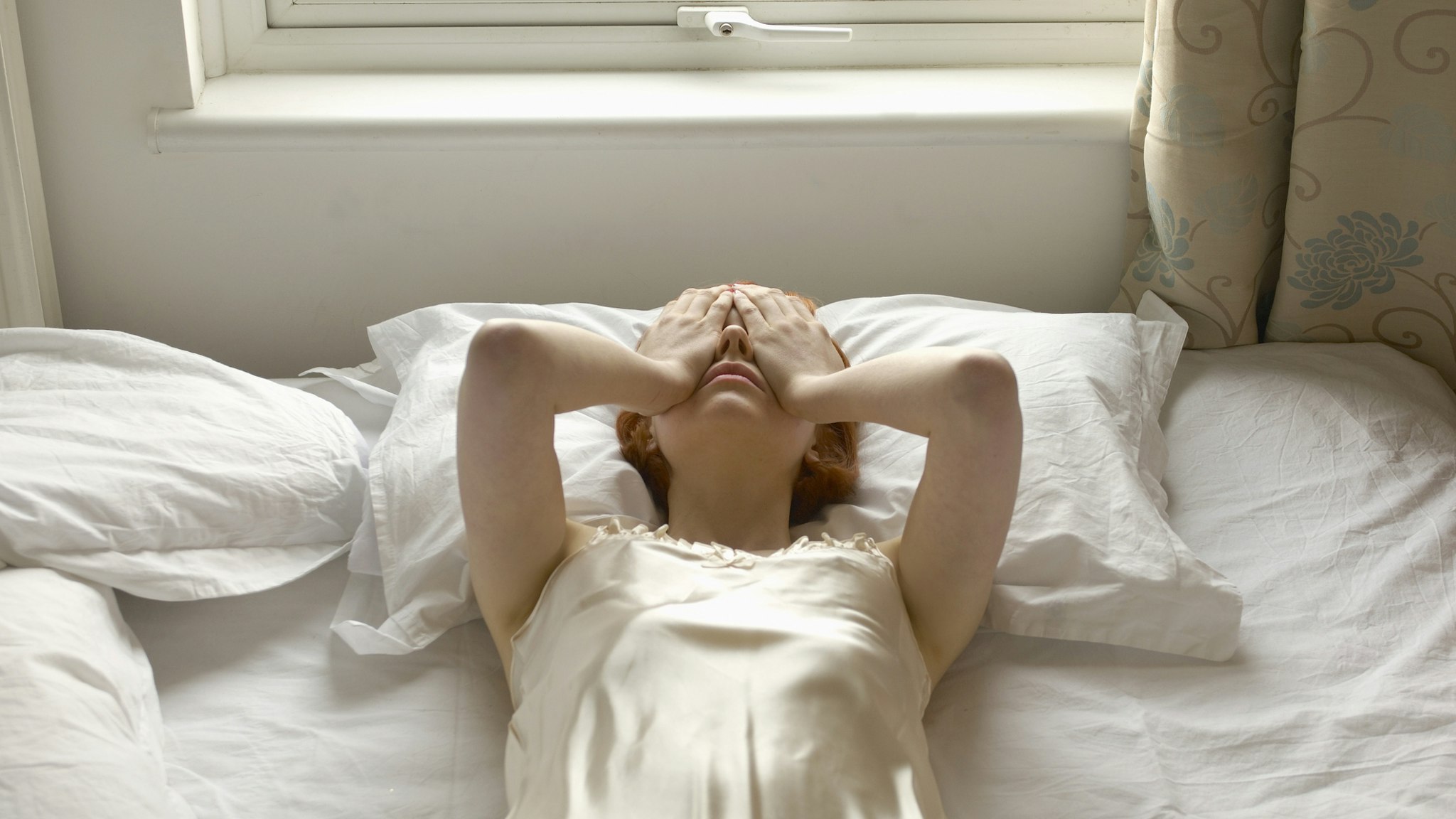 woman on bed with hands over eyes - stock photo
