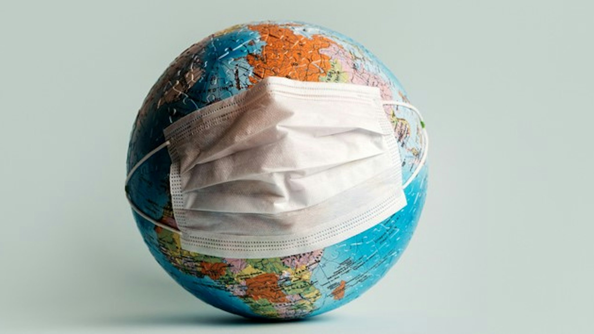 Globe made of jigsaw puzzles with a protective medical mask as a prophylaxis in the fight against coronavirus infection. Measures against the spread of the virus