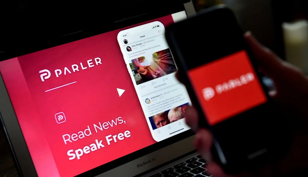 This illustration picture shows social media application logo from Parler displayed on a smartphone with its website in the background in Arlington, Virginia on July 2, 2020. - Amid rising turmoil in social media, recently formed social network Parler is gaining with prominent political conservatives who claim their voices are being silenced by Silicon Valley giants. Parler, founded in Nevada in 2018, bills itself as an alternative to "ideological suppression" at other social networks. (Photo by Olivier DOULIERY / AFP) (Photo by