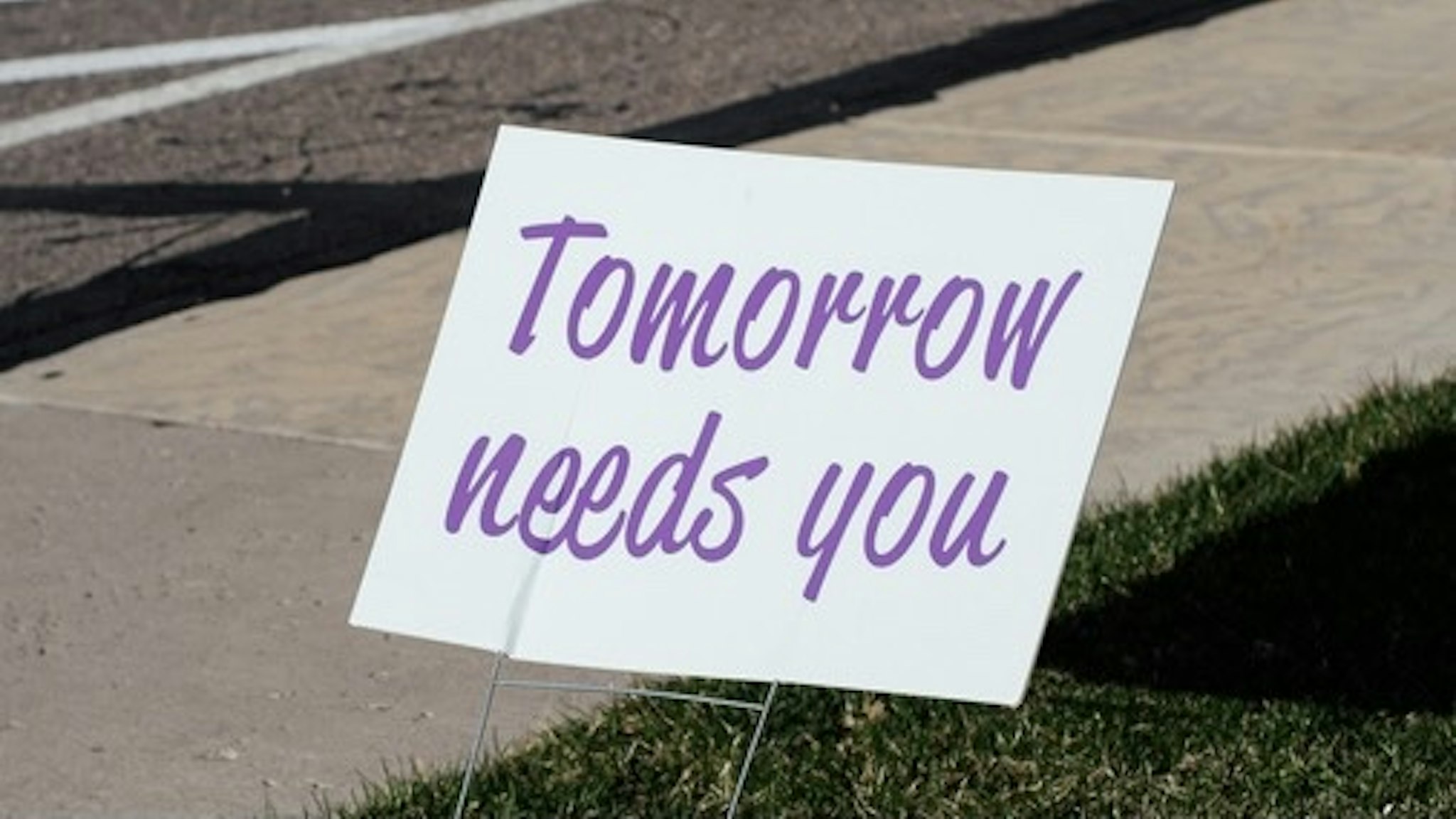 Sign that reads "Tomorrow needs you" placed by a sidewalk. - stock photo