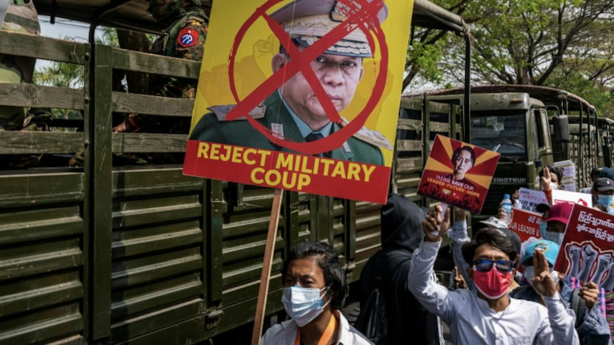 YANGON, MYANMAR - FEBRUARY 15: Protesters hold banners and shout slogans while marching past Myanmar military soldiers who arrived to guard the Central Bank overnight on February 15, 2021 in Yangon, Myanmar. The U.S. Embassy in Myanmar told Americans in Myanmar to "shelter in place" in an announcement after military movements and reports of possible interruptions to telecoms overnight. Armored vehicles were seen on the streets of Myanmar's capital, but protesters turned out in force despite the military presence. (Photo by Hkun Lat/Getty Images)