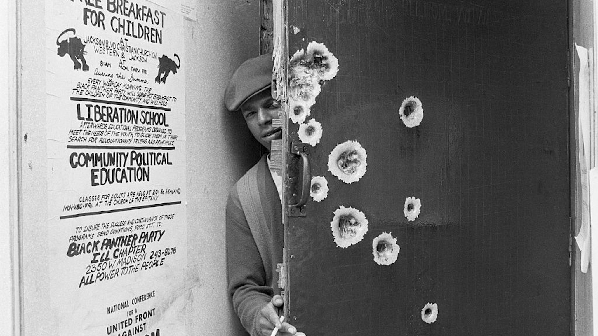 An unidentified member of the militant Black Panthers peeks around a bullet pocked door which police blasted with gunfire early July 31st during a predawn raid. The police broke into the building after several policemen were injured by gunfire coming from the building's upper windows.