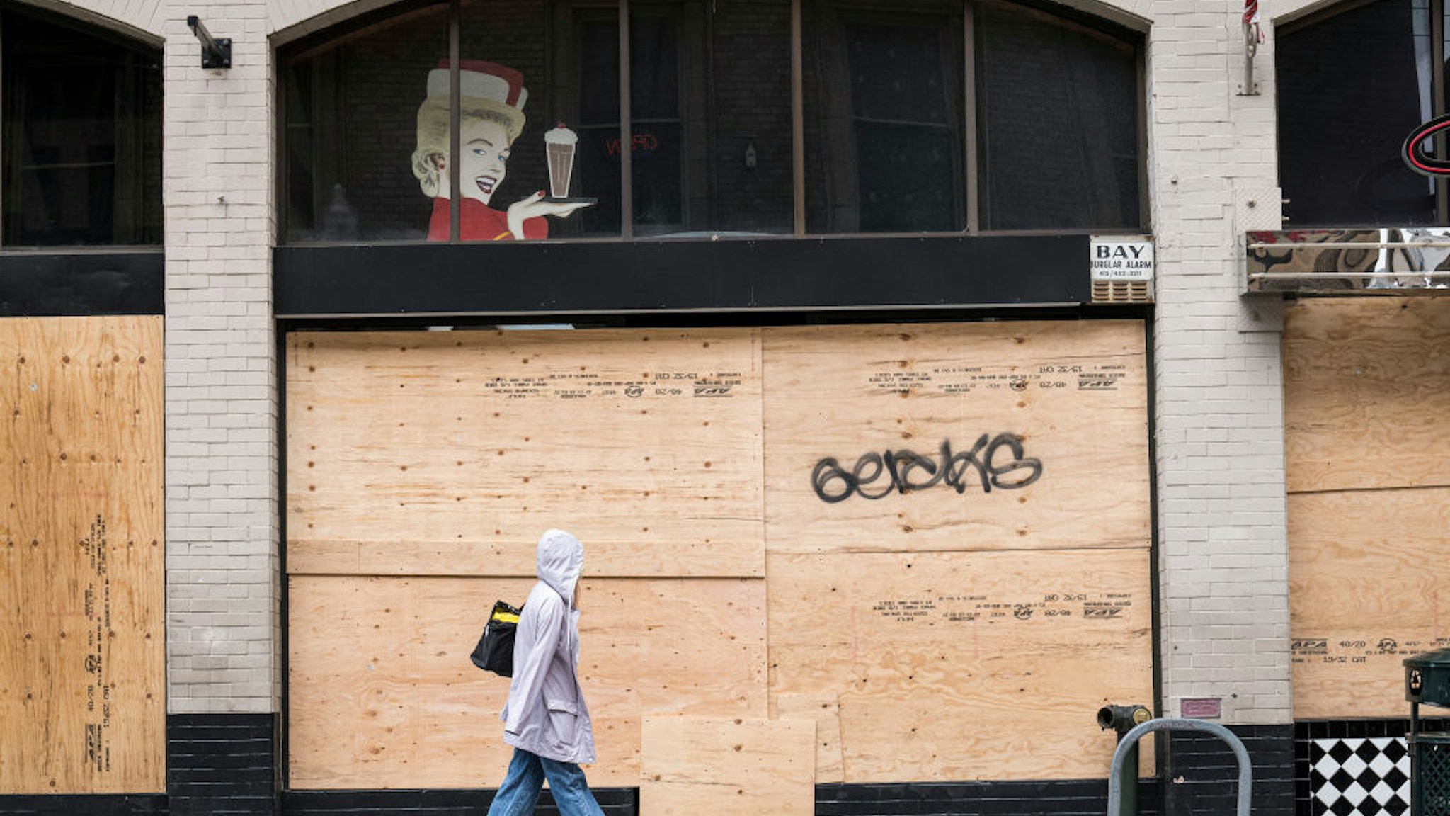 A pedestrian walks past a boarded up Lori's Diner in San Francisco, California, U.S., on Tuesday, March 24, 2020. Governors from coast to coast Friday told Americans not to leave home except for dire circumstances and ordered nonessential business to shut their doors.