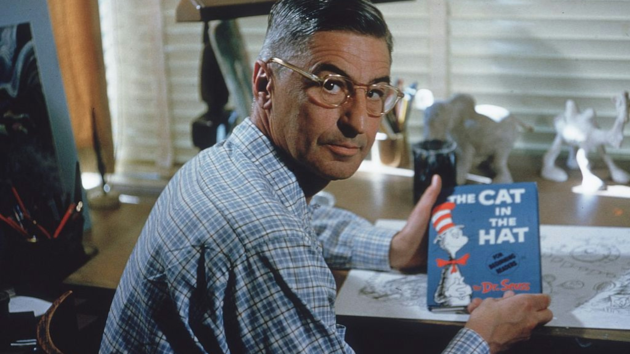 American author and illustrator Dr Seuss (Theodor Seuss Geisel, 1904 - 1991) sits at his drafting table in his home office with a copy of his book, 'The Cat in the Hat', La Jolla, California, April 25, 1957.