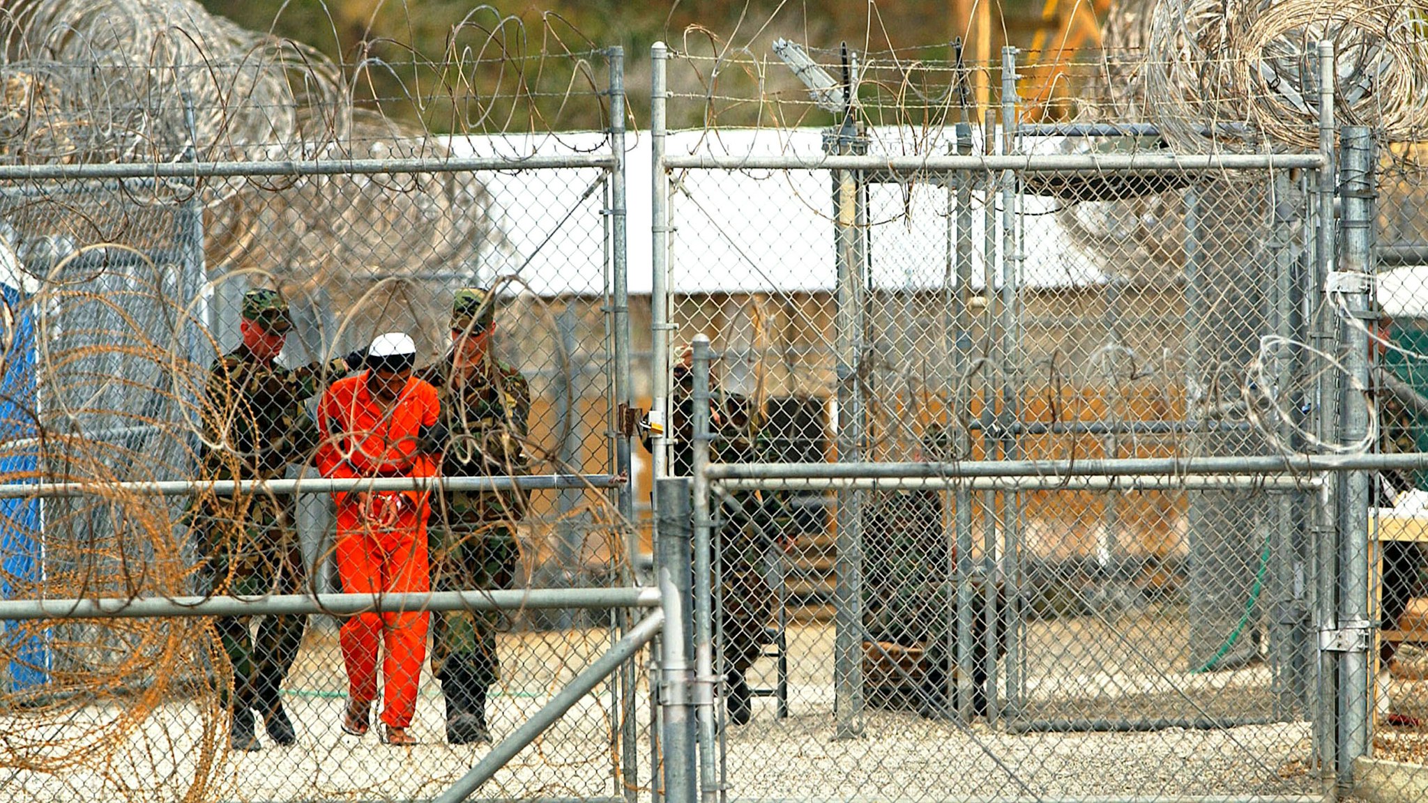 400671 17: Marines transport a detainee behind layers of fencing and razorwire in Camp X-Ray February 6, 2002 in Guantanamo Bay, Cuba. Some of the 156 Al-Qaeda or Taliban detainees are transported periodically for interrogations and other events. U.S. President George W. Bush determined February 7 that the Geneva Convention applies to the conflict in Afghanistan and Taliban soldiers, but not al-Qaeda fighters and other terrorists, the White House said.