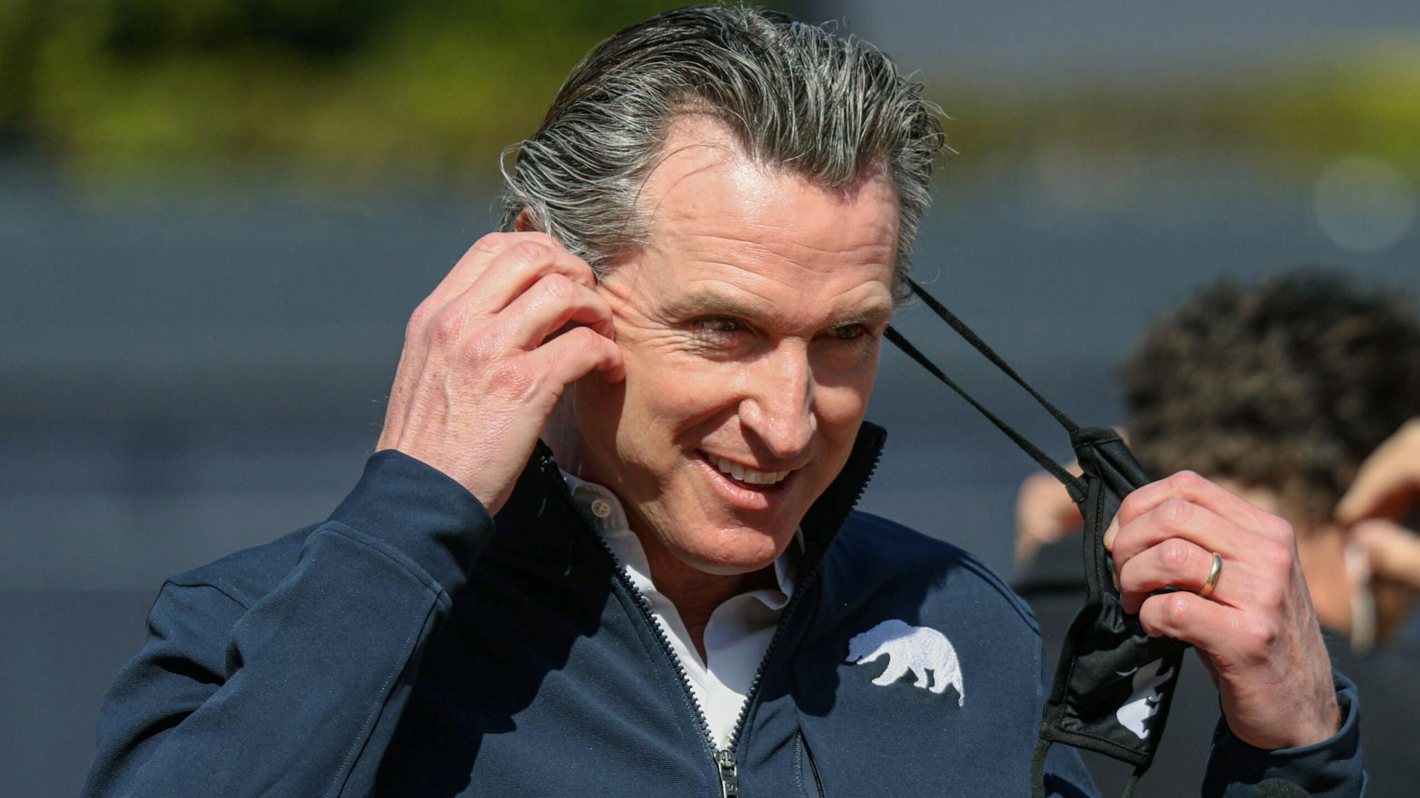 US-HEALTH-VIRUS-VACCINE California Governor Gavin Newsom takes off his facemask before speaking to members of the media during a press conference at Petco Park, February 8, 2021 in San Diego, California, during a visit to the Petco Park Vaccination Supersite. - The Petco Park Vaccination Supersite, which is hosted in a parking lot next to the ballpark, is a partnership between San Diego County, the San Diego Padres baseball team and UC San Diego Health and has capacity to dole out about 5,000 COVID-19 vaccines per day.