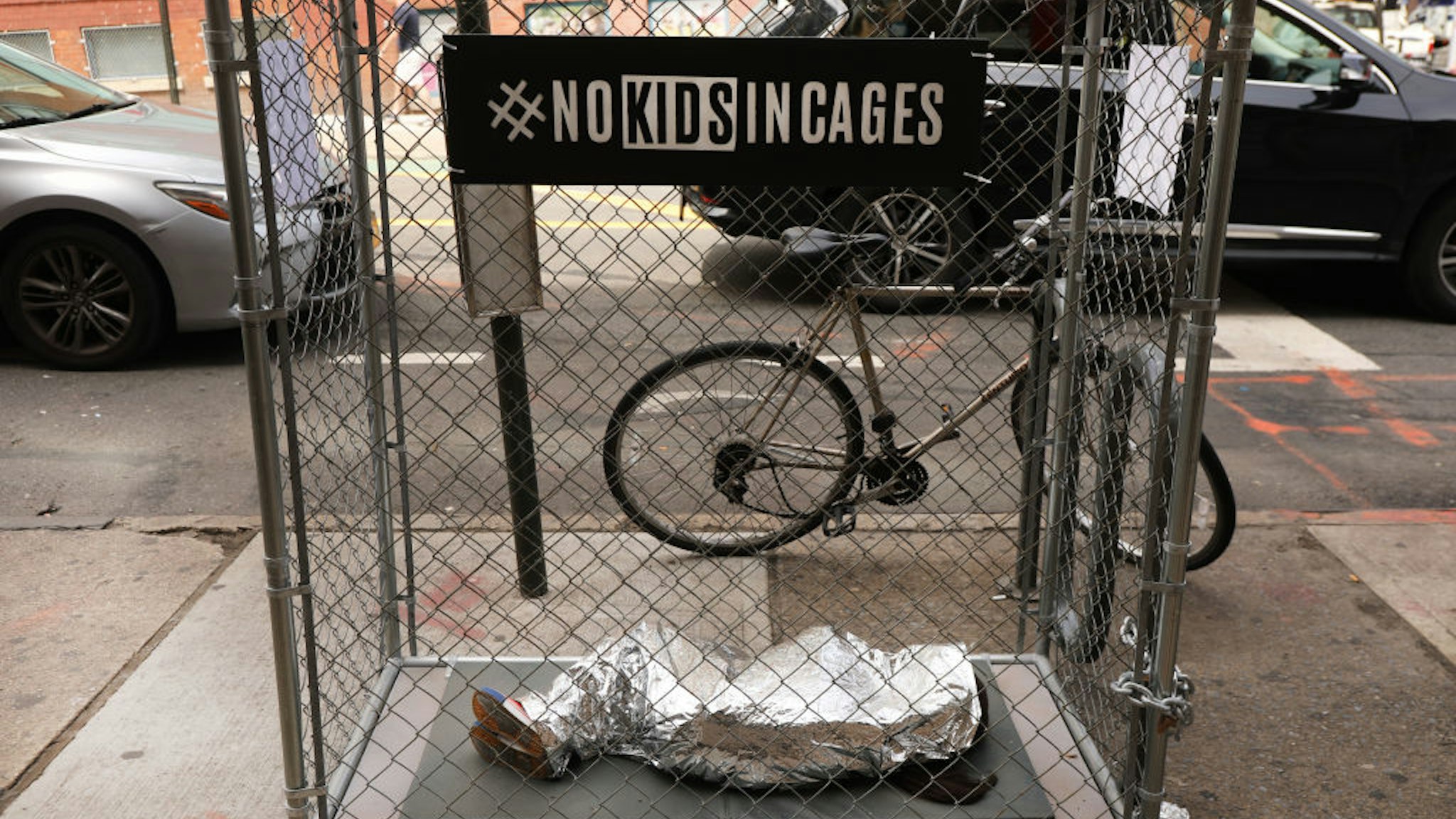 A pop-up art installation depicting a small child curled up underneath a foil survival blanket in a chain-link cage stands along a Brooklyn street on June 12, 2019 in New York City.