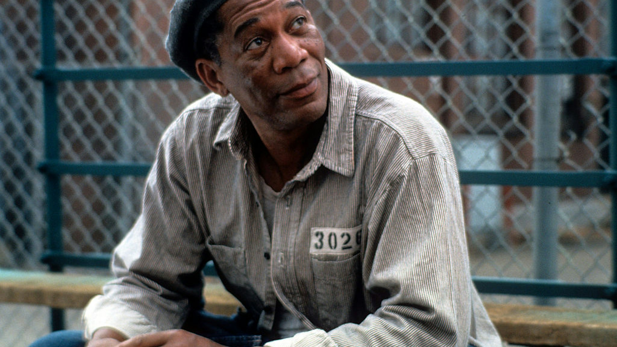 Morgan Freeman sitting outside with a hat and prison uniform on in a scene from the film 'The Shawshank Redemption', 1994. (Photo by Castle Rock Entertainment/Getty Images)