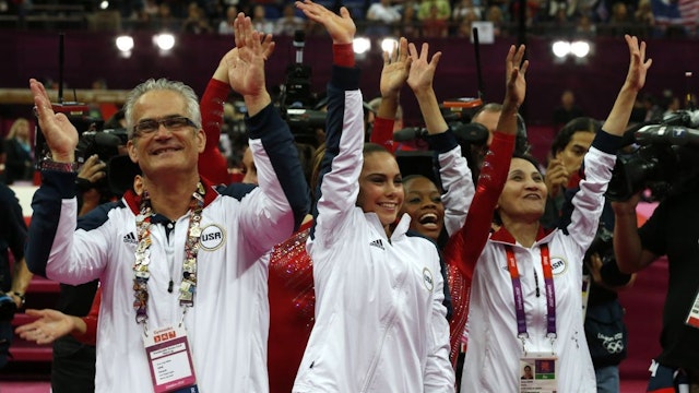 US gymnasts Gabrielle Douglas (C), Mckayla Maroney (2D-L), coaches Jenny Zhang (R) and John Geddert (L) celebrate winning gold in the women's team of the artistic gymnastics event of the London Olympic Games on July 31, 2012 at the 02 North Greenwich Arena in London. Team US won gold, Team Russia took silver and Team Romania got bronze. (Photo by Thomas Coex/AFP Photo/Getty Images)