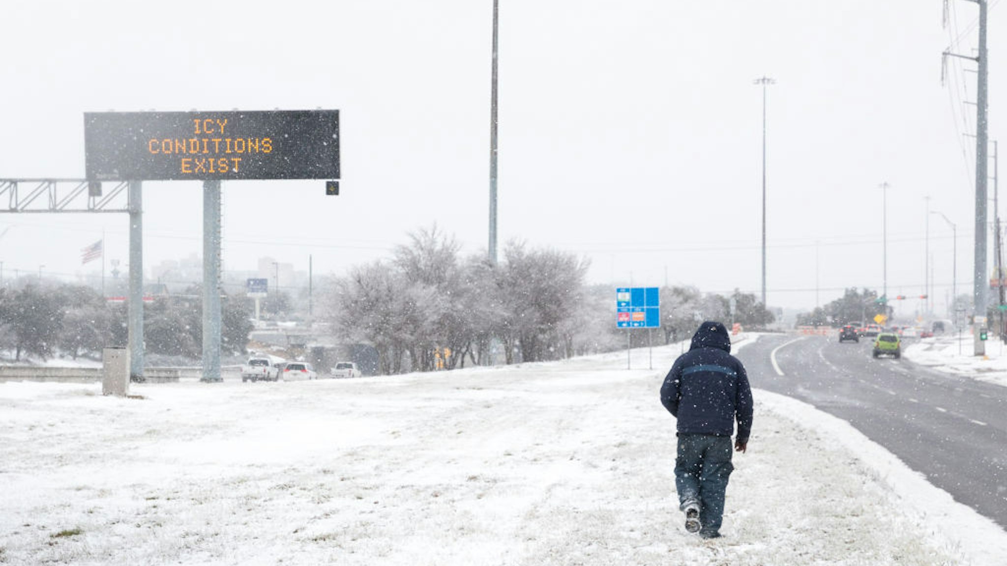 A pedestrians walks past a road sign warning commuters of icy conditions on a road in Austin, Texas, U.S., on Thursday, Feb. 18, 2021. Texas is restricting the flow of natural gas across state lines in an extraordinary move that some are calling a violation of the U.S. Constitutions commerce clause.