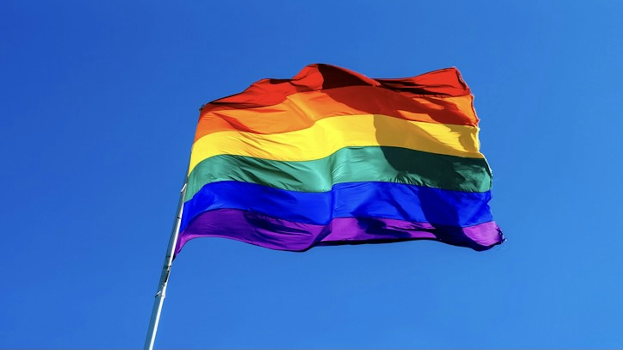 Rainbow flag waving in the wind against clear blue sky - stock photo