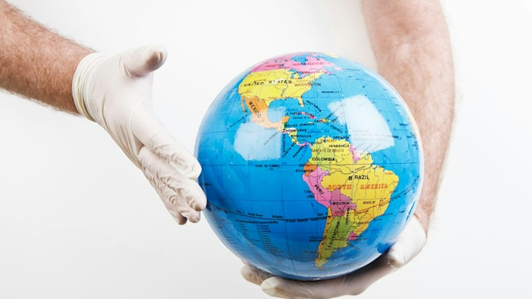 Global health | Doctor wearing gloves holds globe - stock photo