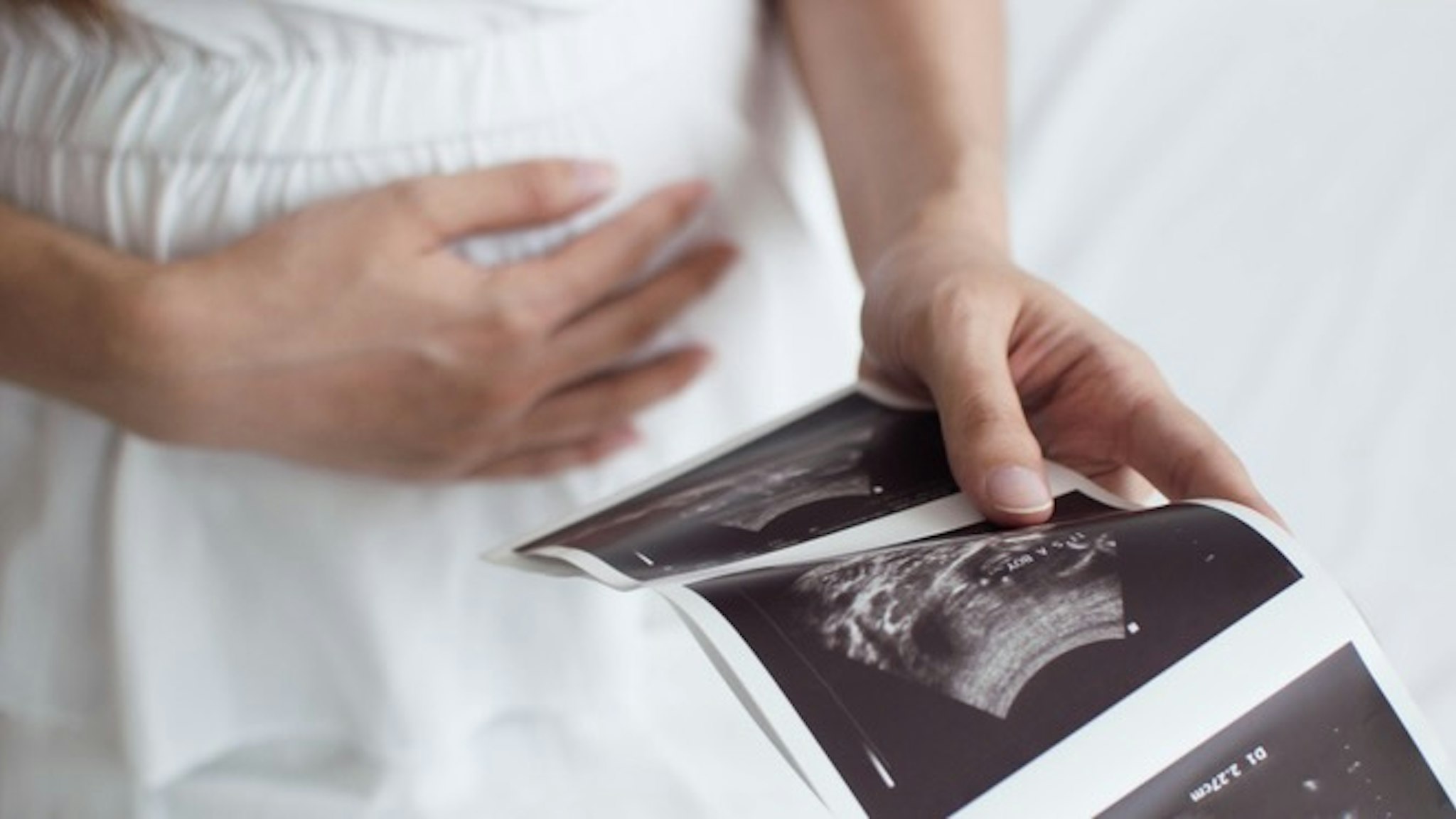 A pregnant woman is holding an ultrasound scan result - stock photo A midsection of a pregnant Southeast Asian woman holding an ultrasound scan result on the bed