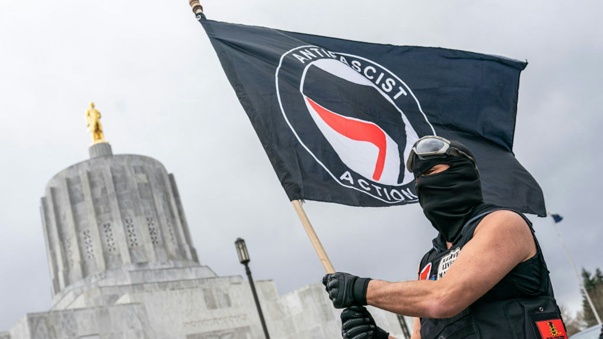 SALEM, OR - MARCH 28: A protester waves an anti-fascist flag at the Oregon statehouse on March 28, 2021 in Salem, Oregon. The protesters clashed with occupants of vehicles that had participated in an American flag-waving car caravan, despite law enforcements efforts to to keep the groups separate. (Photo by Nathan Howard/Getty Images)