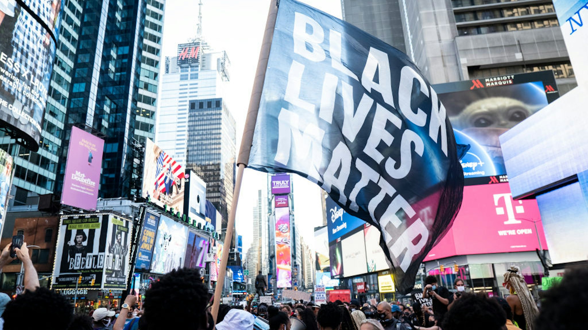 MANHATTAN, NY - July 26: A protester holds a large flag that says, "Black Lives Matter" which is draping the landscape of Times Square in New York. This non-violent protest was a March for Black Womxn which started at Times Square and walked through Manhattan. This is days after Portland and other cities have seen federal agents have taken protesters and put into unmarked vehicles while others have been beaten and pepper sprayed. Protesters continue taking to the streets across America and around the world after the killing of George Floyd at the hands of a white police officer Derek Chauvin that was kneeling on his neck during for eight minutes, was caught on video and went viral. During his arrest as Floyd pleaded, "I Can't Breathe". The protest are attempting to give a voice to the need for human rights for African American's and to stop police brutality against people of color. They are also protesting deep-seated racism in America. Many people were wearing masks and observing social distancing due to the coronavirus pandemic. Photographed in the Manhattan Borough of New York on July 26, 2020, USA.