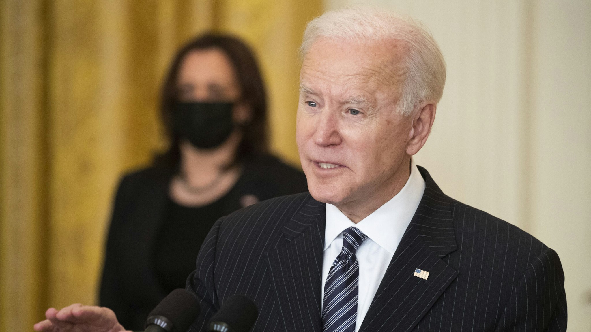 U.S. President Joe Biden speaks while delivering an address as U.S. Vice President Kamala Harris, left, listens in the East Room of the White House in Washington, D.C., U.S., on Thursday, March 18, 2021. Biden announced the U.S. on Friday will clinch his goal of administering 100 million Covid-19 vaccine shots in the first 100 days of his presidency, reaching the mark six weeks ahead of time.