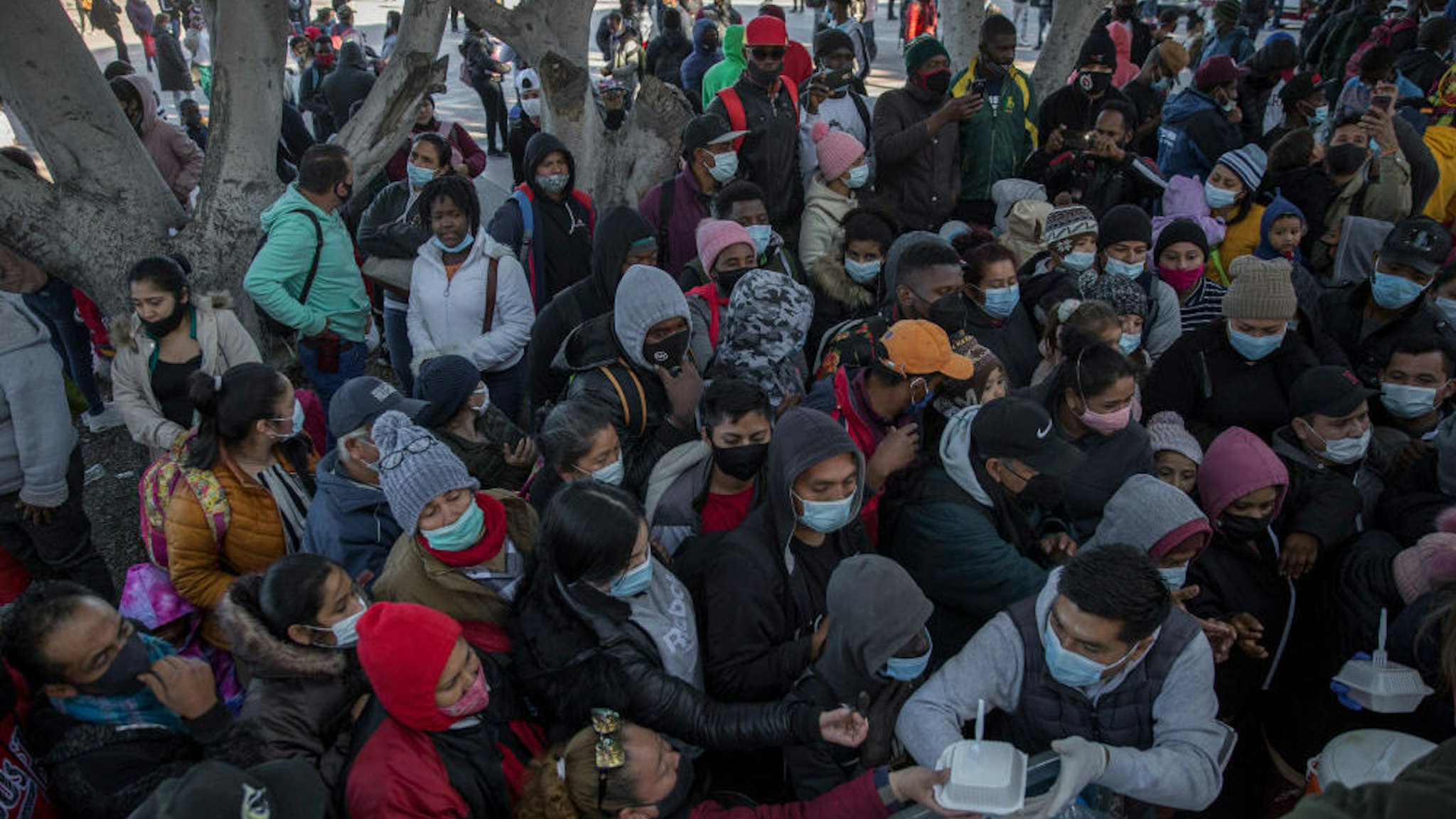 19 February 2021, Mexico, Tijuana: Numerous migrants wearing masks gather and wait for food and water to be distributed at the border crossing. Following the announced change of direction in US migration policy, numerous migrants have gathered at the border between Mexico and the US, hoping to gain entry to the US. With the new regulation US President Biden's administration is breaking with the restrictive immigration policy of his predecessor Trump. Photo: Stringer/dpa
