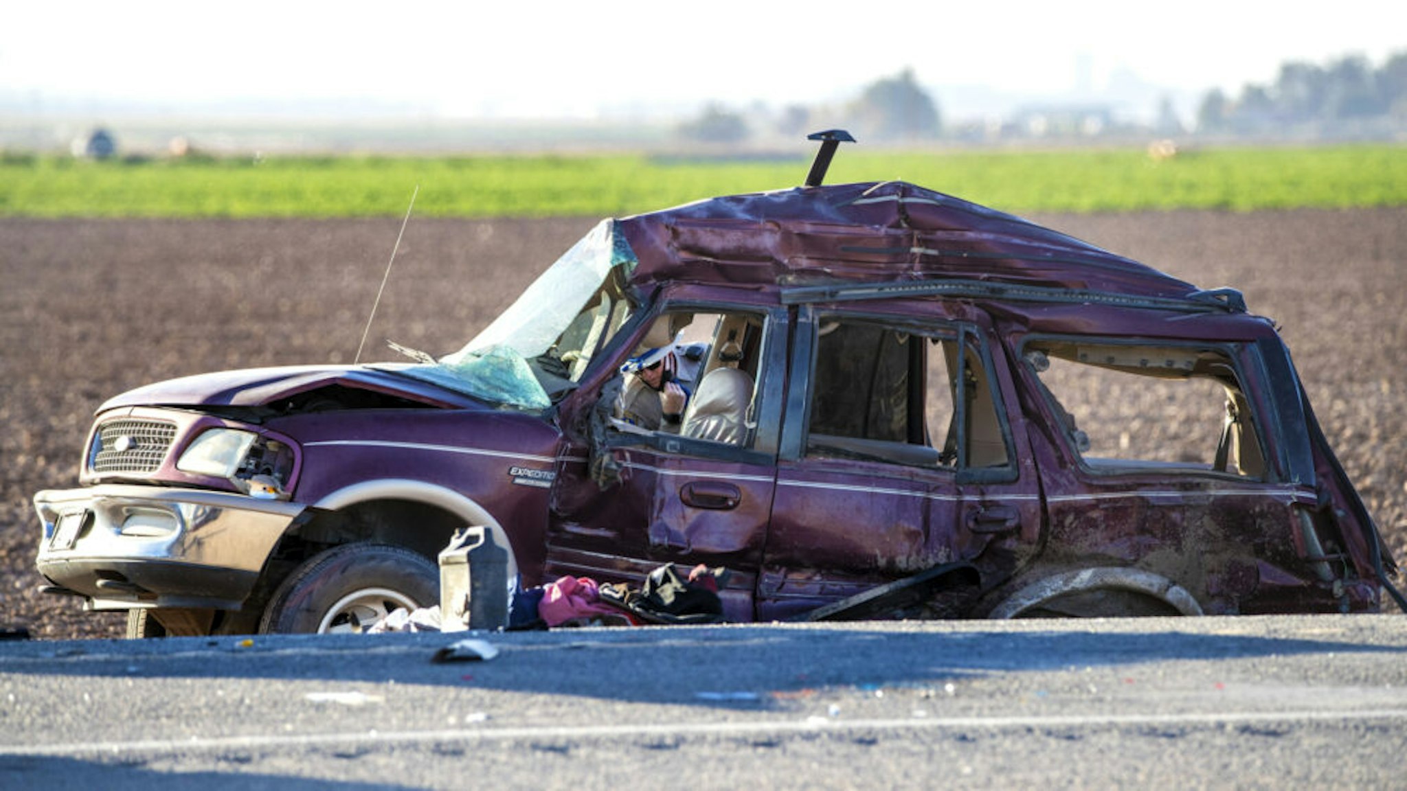 HOLTVILLE, CA - MARCH 2, 2021: A CHP officer looks inside a mangled SUV which was carrying 25 people when it collided with a semi-truck killing 13 on Highway 115 near the Mexican border on March 2, 2021 in Holtville, California. All the back seats had beens stripped form the vehicle. The passengers in the SUV ranged in age form 15-53.
