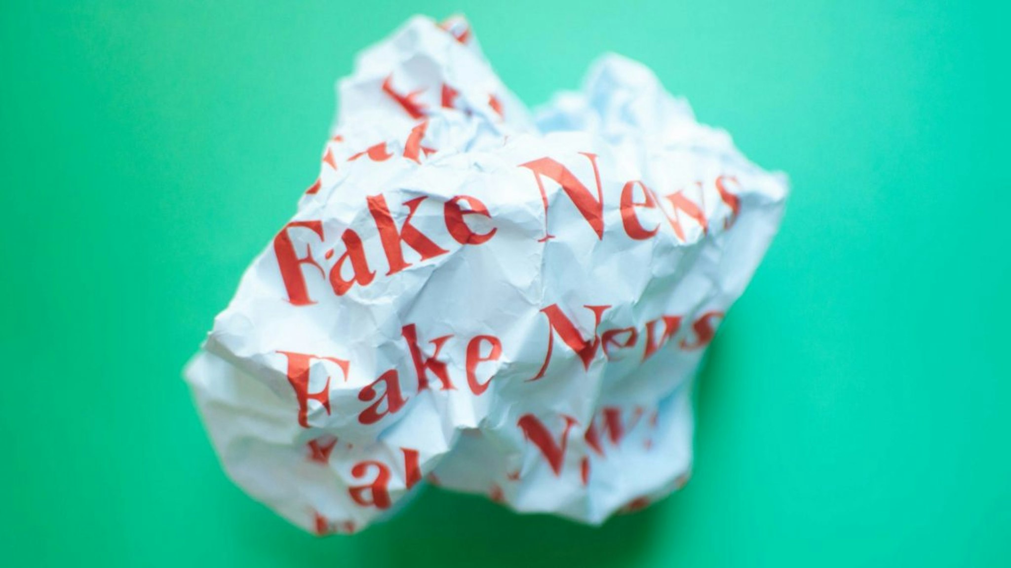 Crumpled paper with red font fake news against blue green background.