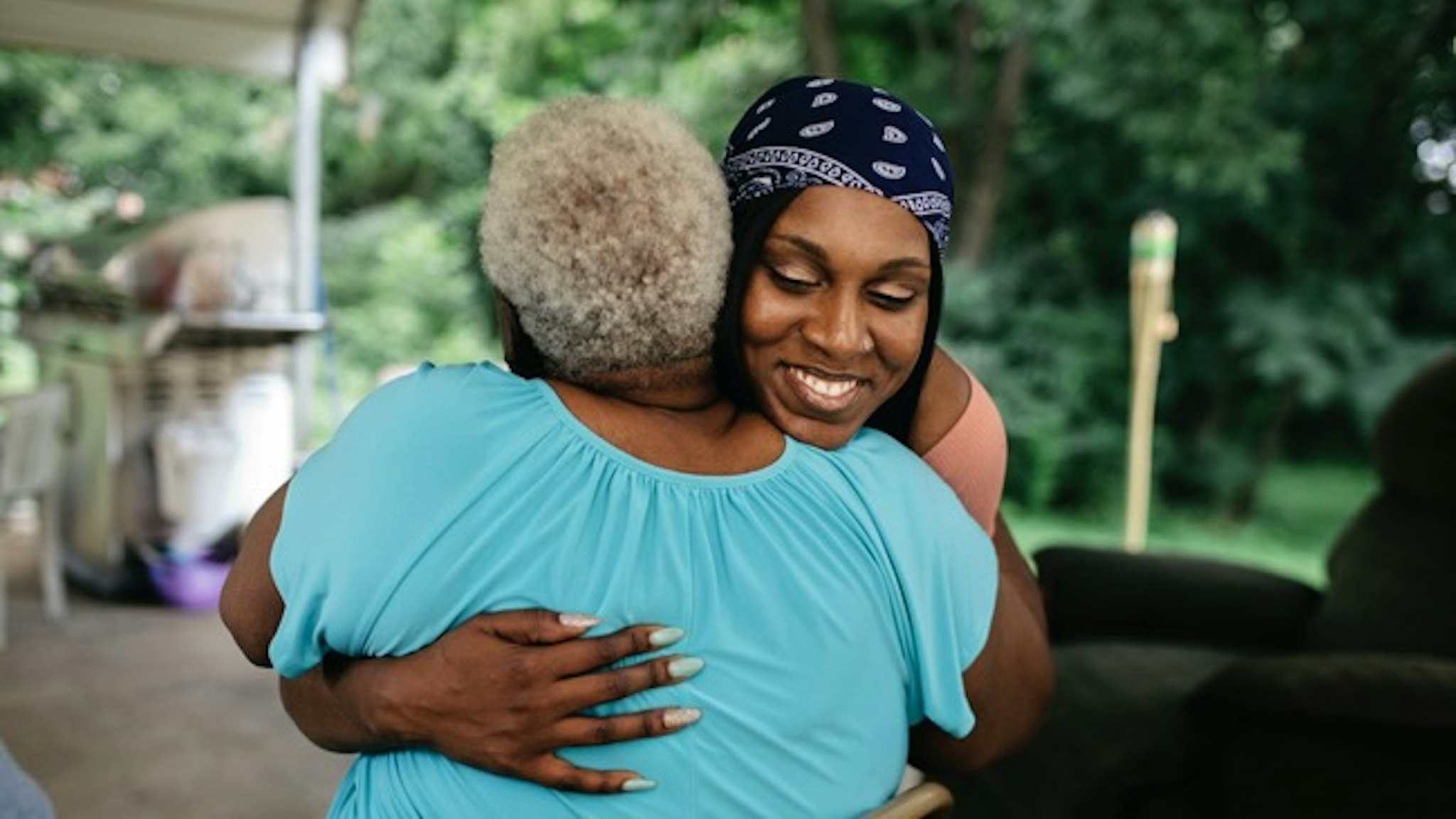 Young black woman hugging senior family member - stock photo Young black woman hugging senior family member. Family is out doors at a cookout."nMembers of a black middle class America family.