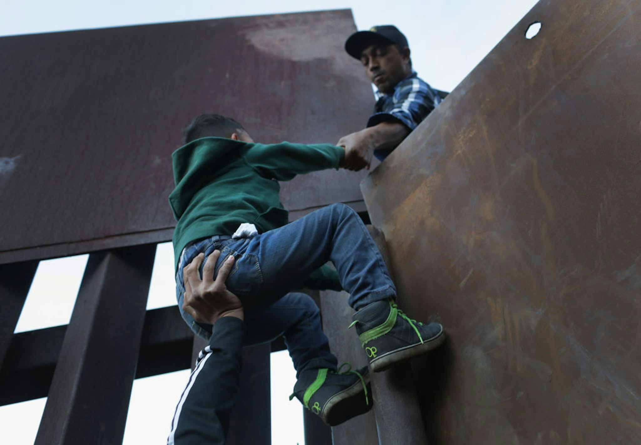 TIJUANA, MEXICO - DECEMBER 02: A boy is hoisted by fellow members of the migrant caravan over the U.S.-Mexico border fence on December 2, 2018 from Tijuana, Mexico. Numerous members of the caravan were able to cross over from Tijuana to San Diego and were quickly taken into custody by U.S. Border Patrol agents. Most had planned to request political asylum in the United States after traveling more than 6 weeks from Central America. (Photo by John Moore/Getty Images)
