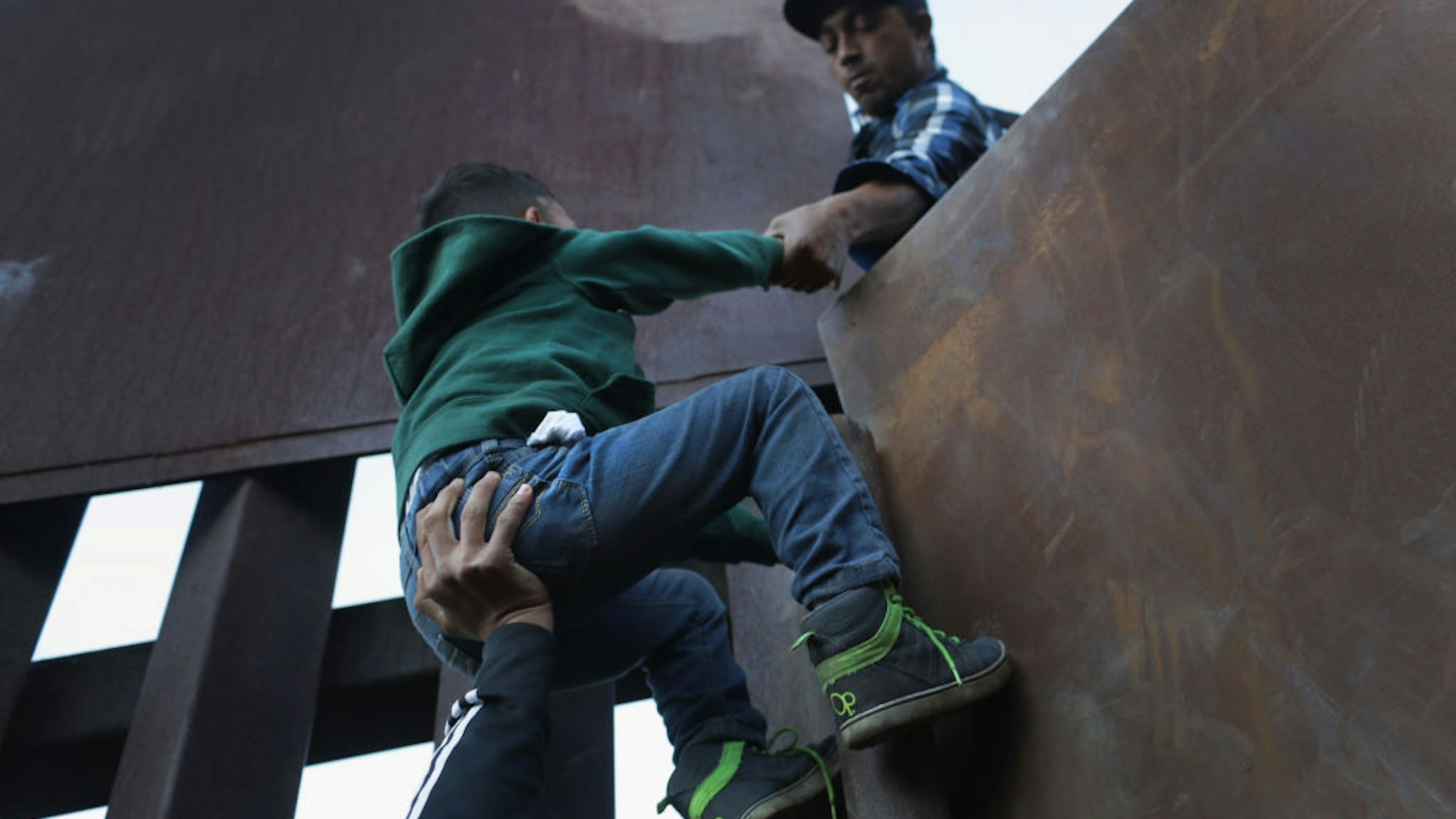 TIJUANA, MEXICO - DECEMBER 02: A boy is hoisted by fellow members of the migrant caravan over the U.S.-Mexico border fence on December 2, 2018 from Tijuana, Mexico. Numerous members of the caravan were able to cross over from Tijuana to San Diego and were quickly taken into custody by U.S. Border Patrol agents. Most had planned to request political asylum in the United States after traveling more than 6 weeks from Central America. (Photo by John Moore/Getty Images)
