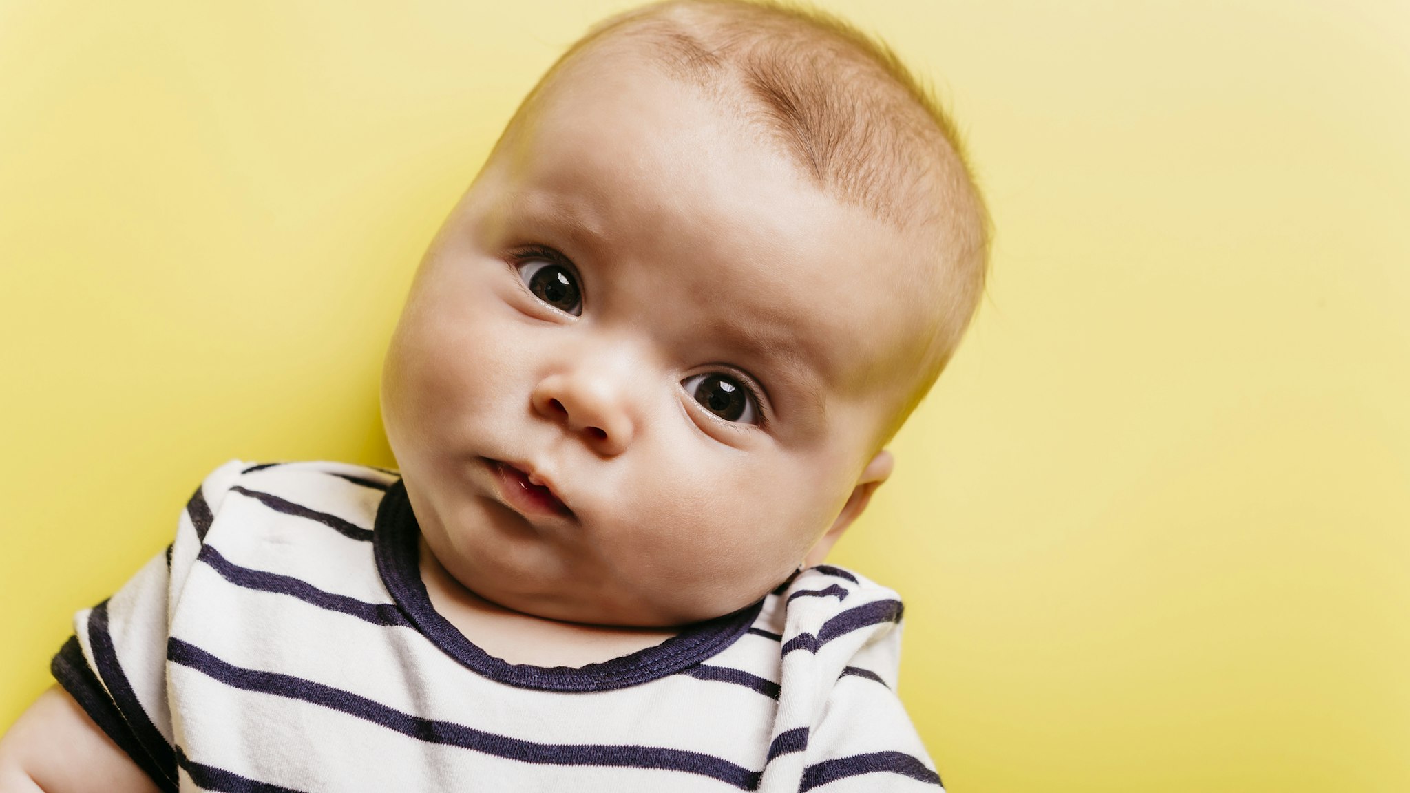 Portrait of sceptical baby girl in front of yellow background - stock photo