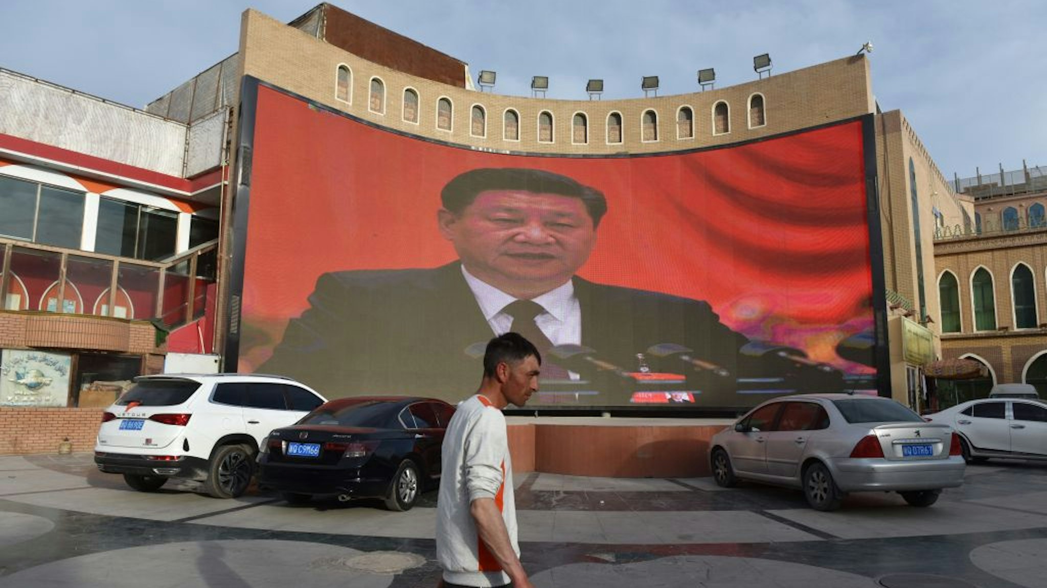 This photo taken on June 4, 2019 shows a man walking past a screen showing images of China's President Xi Jinping in Kashgar in China's northwest Xinjiang region. - China has enforced a massive security crackdown in Xinjiang, where more than one million ethnic Uighurs and other mostly Muslim minorities are believed to be held in a network of internment camps that Beijing describes as "vocational education centres" aimed at steering people away from religious extremism. (Photo by Greg Baker / AFP) (Photo credit should read GREG BAKER/AFP via Getty Images)
